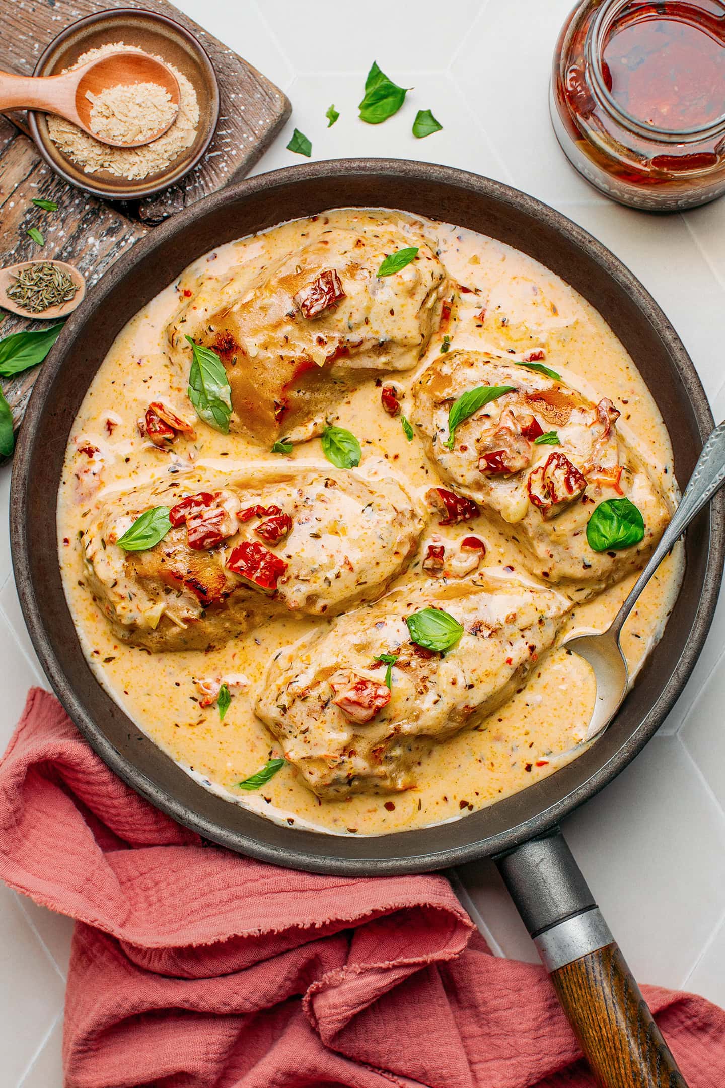 Vegan chicken coated in a creamy sauce and topped with chopped sun-dried tomatoes in a skillet.