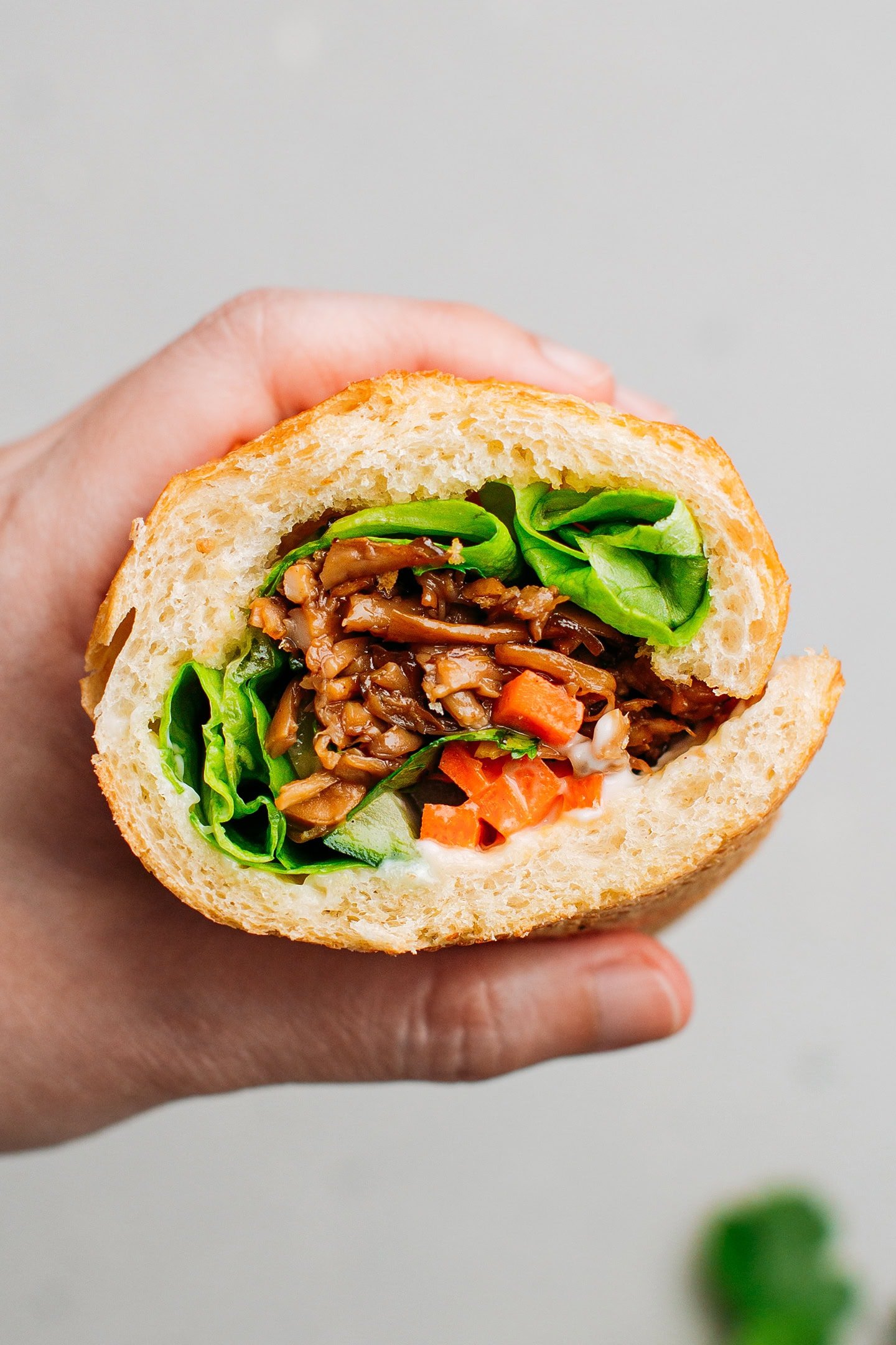 Holding a half of banh mi filled with mushrooms, carrot pickles, mayo, and lettuce.