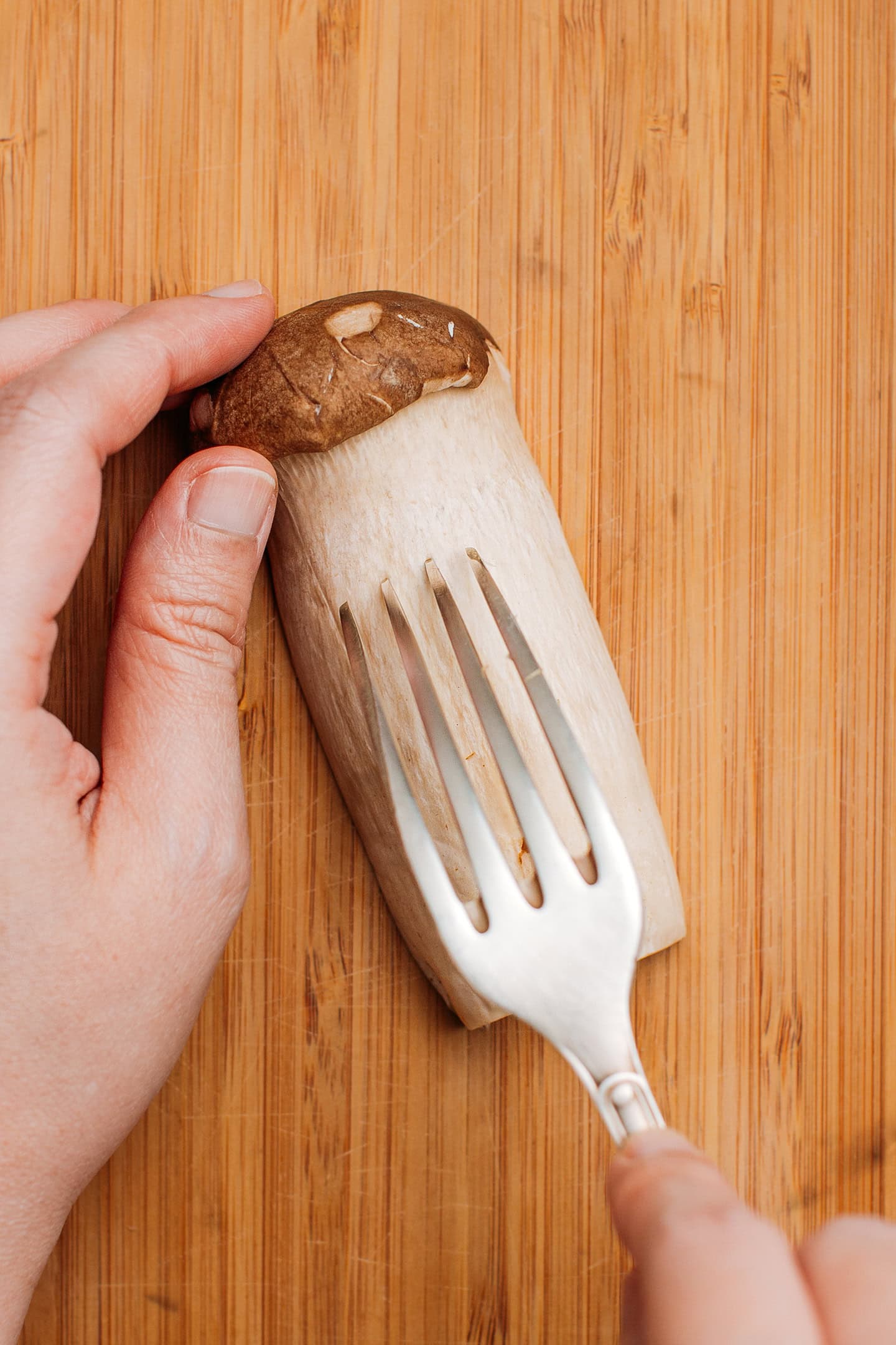 Shredding king oyster mushrooms using a fork.