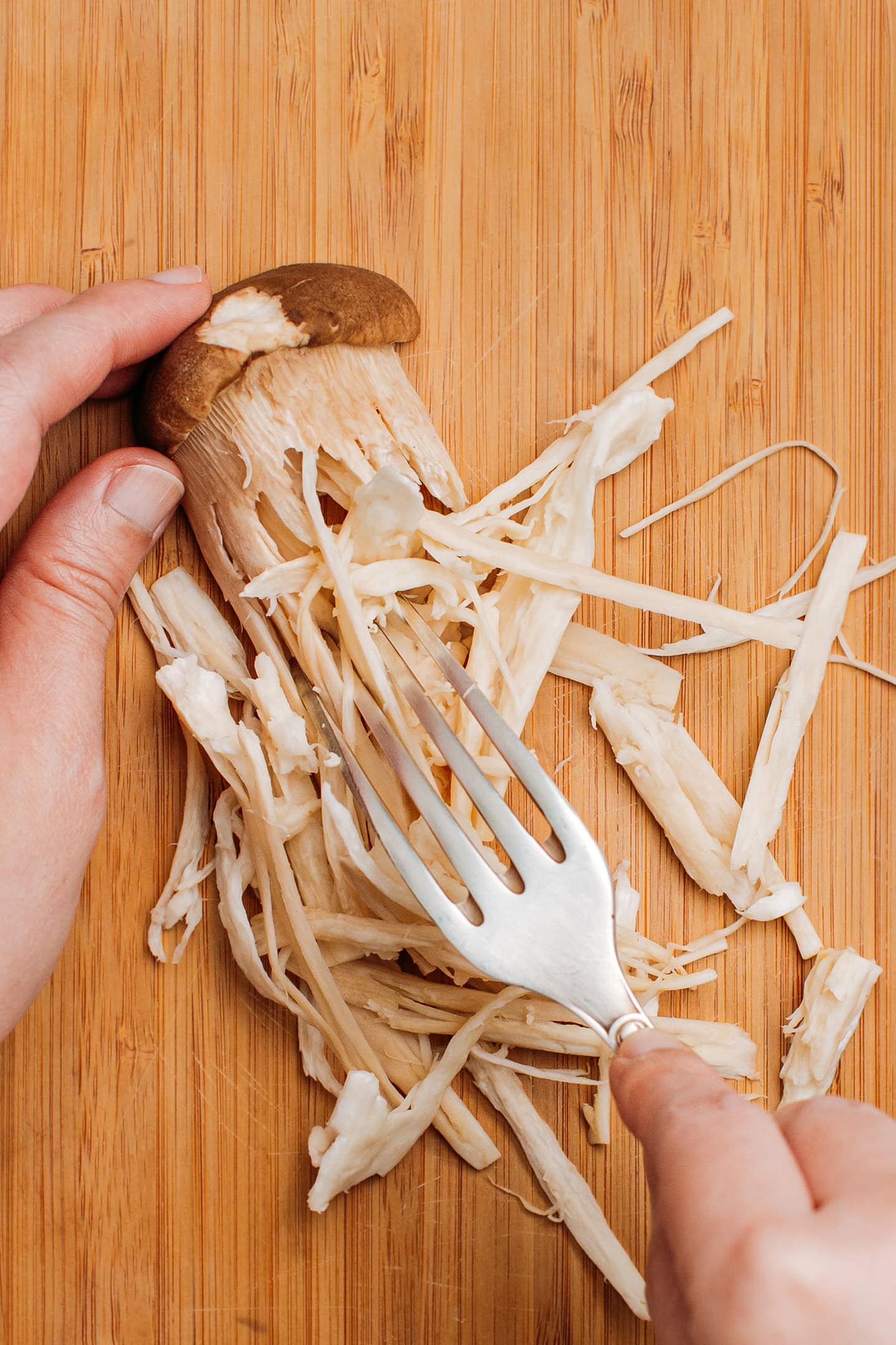 Shredding king oyster mushrooms into strips using a fork.