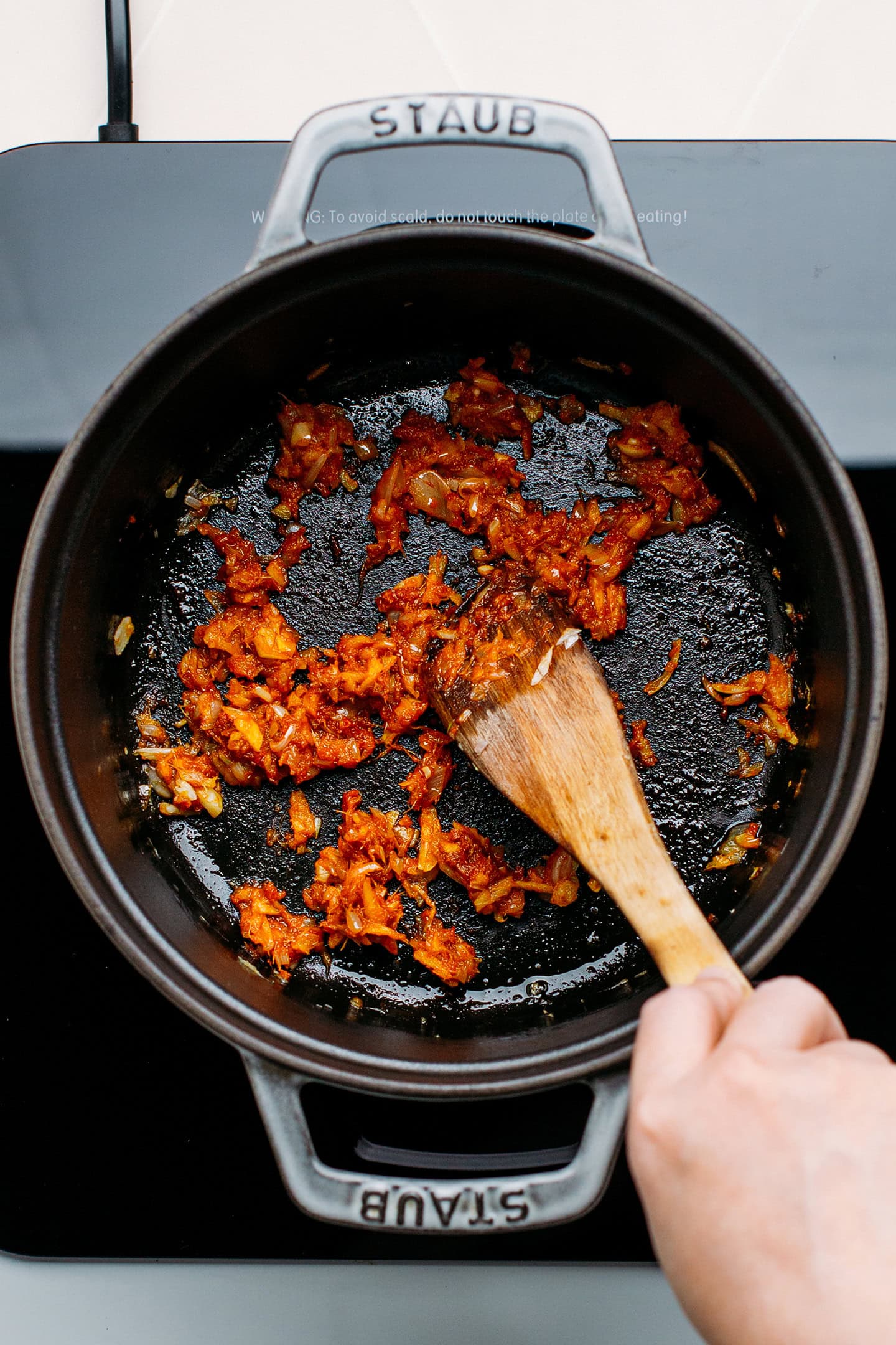 Sautéed garlic, shallots, ginger, and red curry paste in a pot.