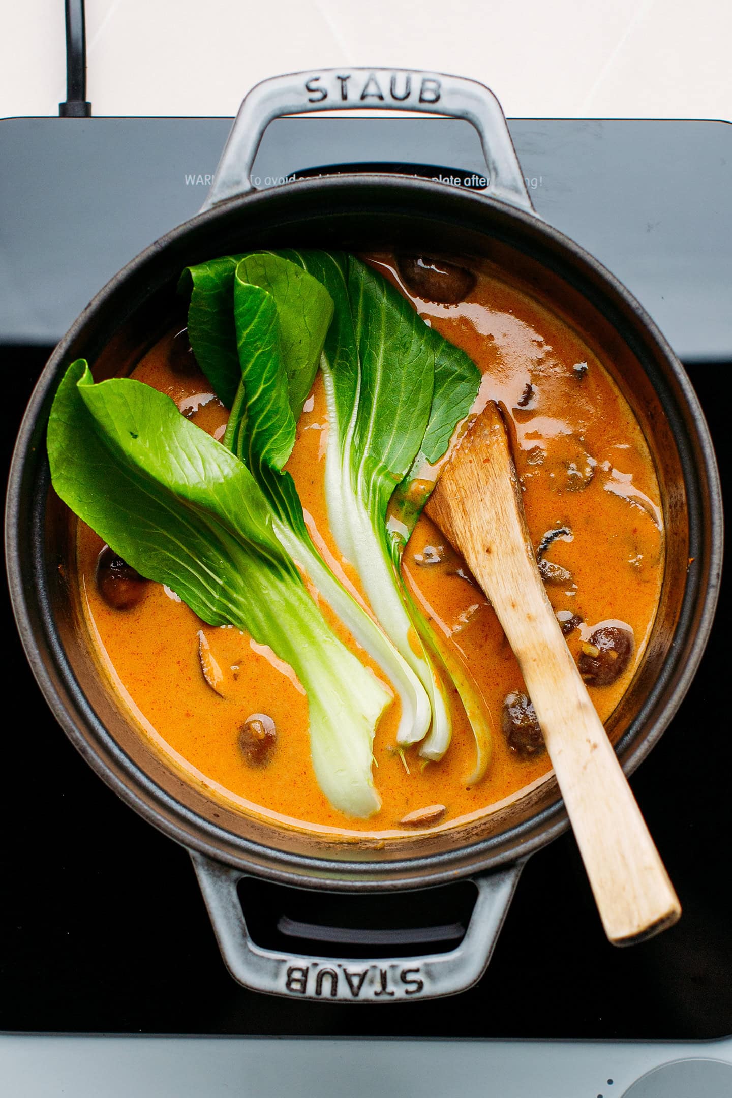 Red curry with pak choy and mushrooms in a pot.