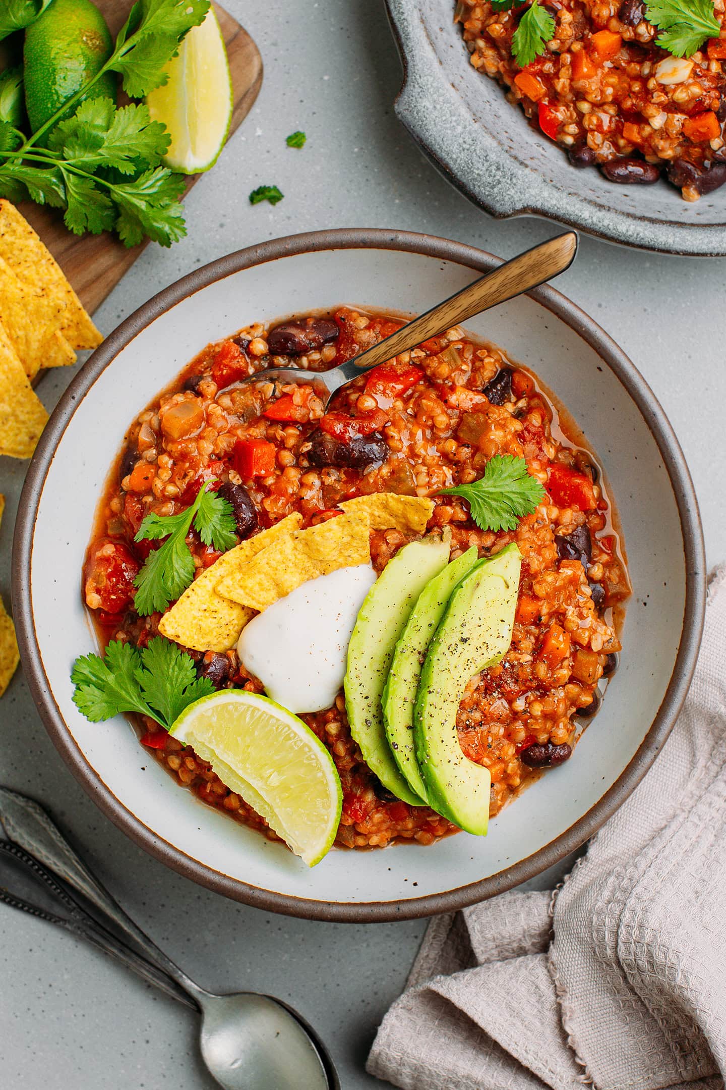 Bowl of buckwheat chili topped with avocado slices, coconut cream, and tortilla chips.