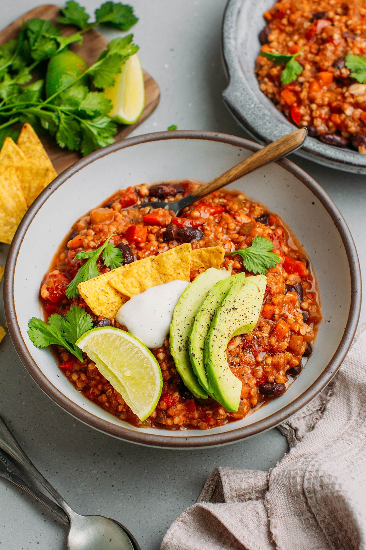 Bowl filled with buckwheat groats chili, avocado slices, tortilla chips, and cilantro.