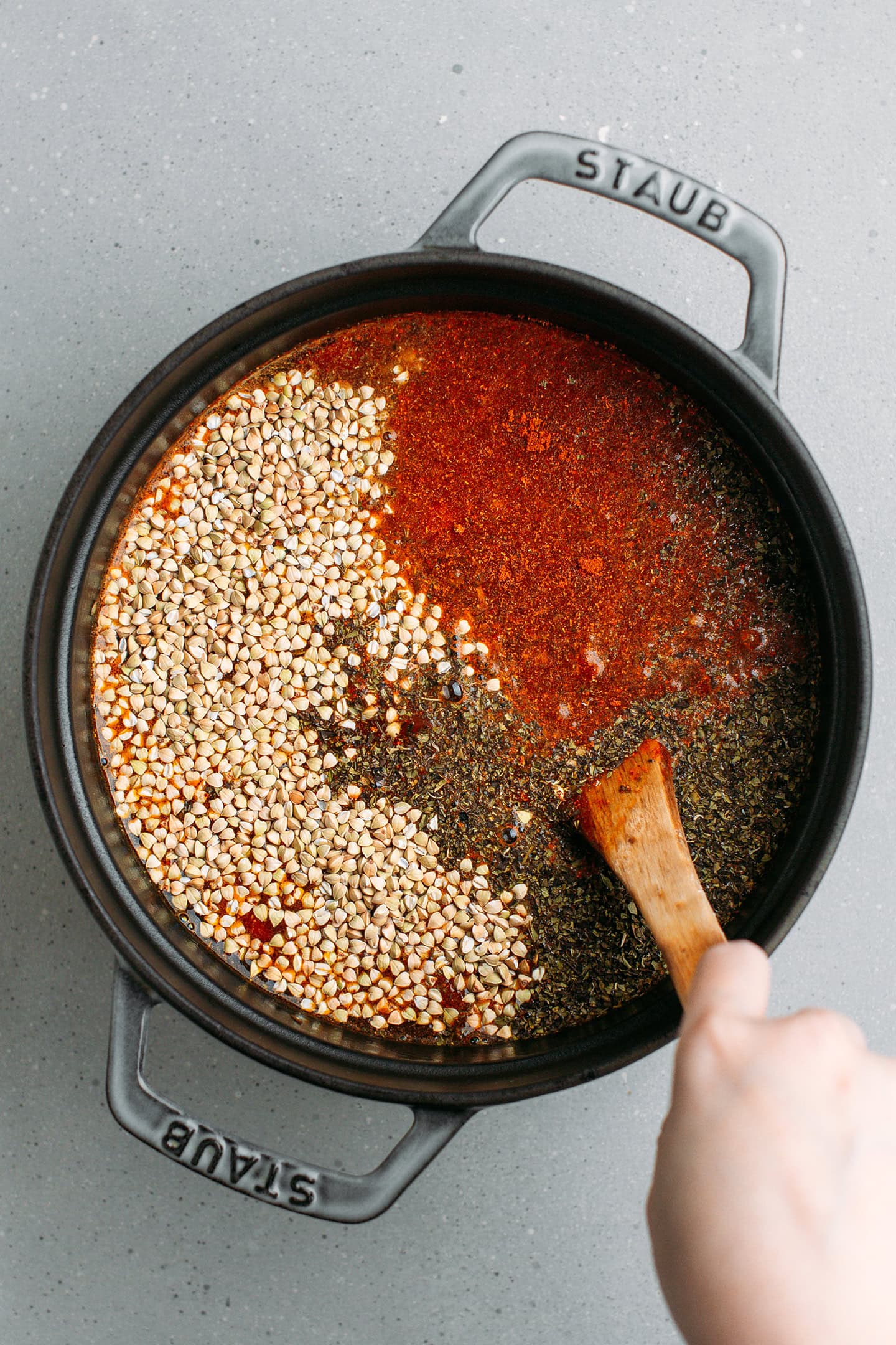 Stirring buckwheat groats with diced tomatoes in a pot.