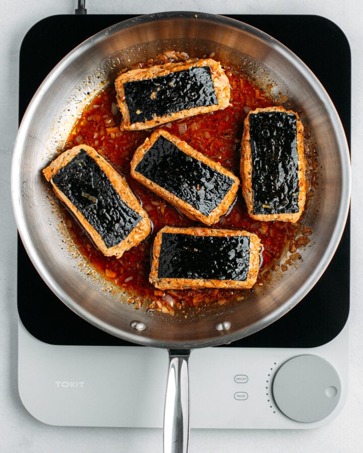 Five pieces of vegan fish in a skillet with black pepper sauce.