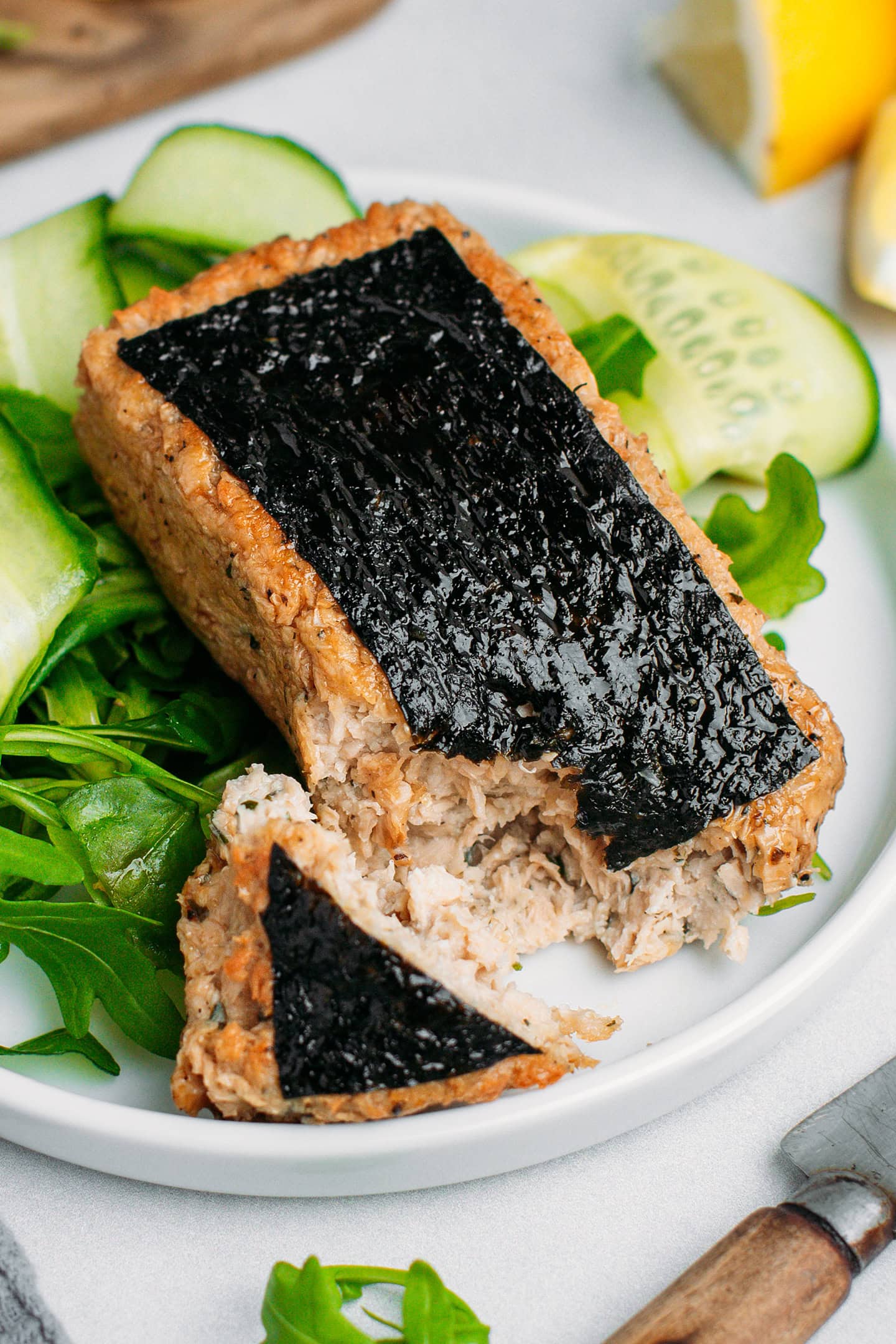 Vegan fish fillet with nori seaweed on a plate filled with green vegetables.