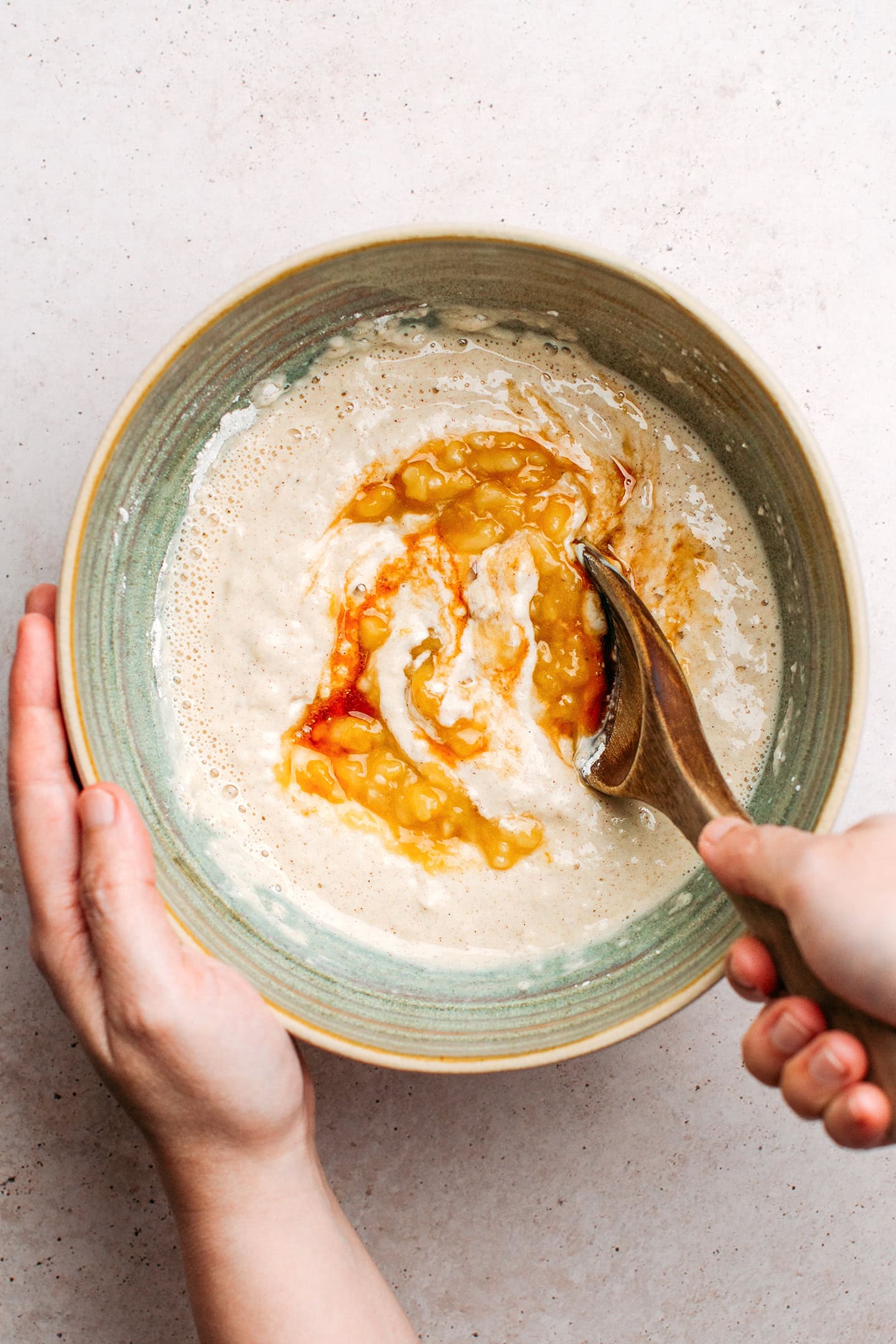 Incorporating mashed bananas into a pancake batter in a mixing bowl.