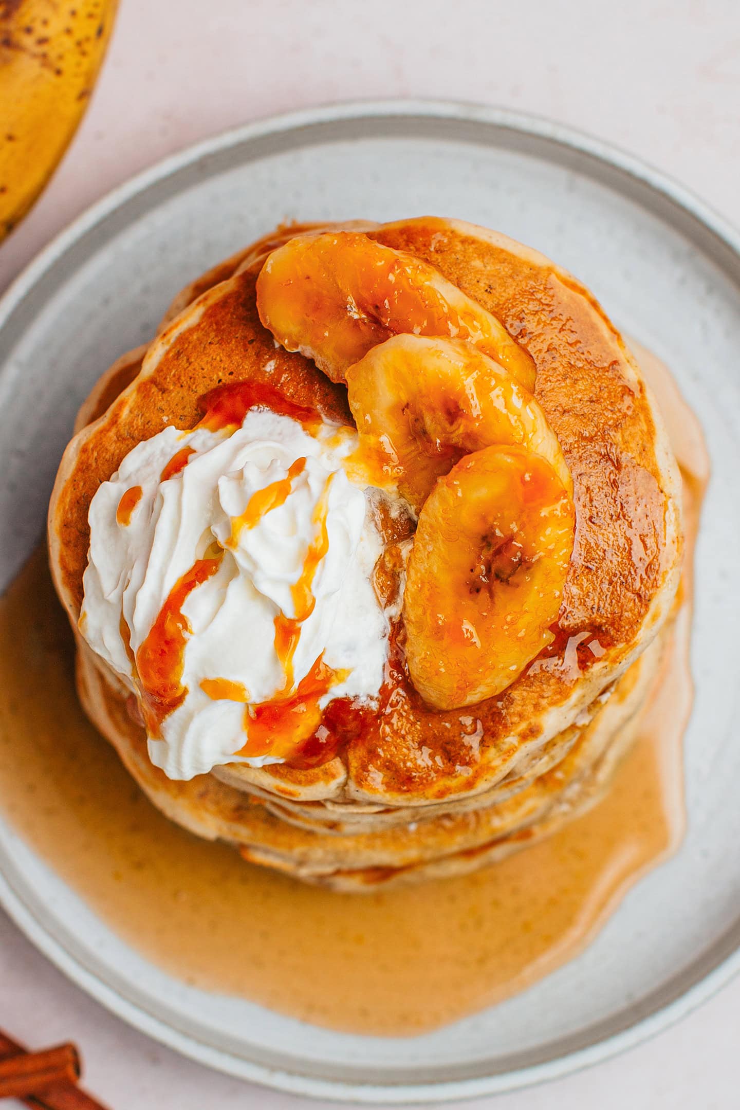 Top view of banana pancakes topped with vegan whipping cream and caramelized bananas.