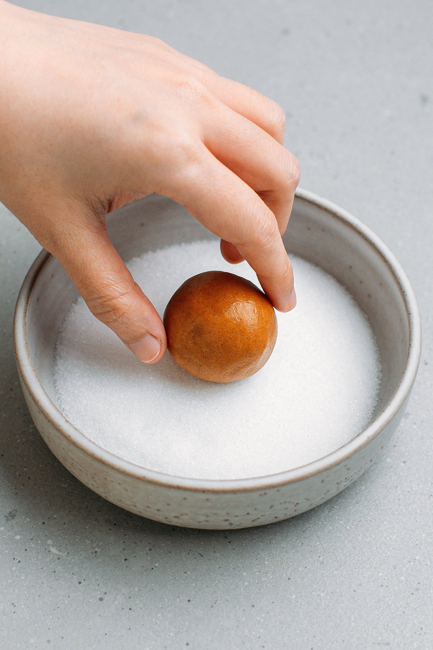 Rolling a ball of cookie dough in granulated sugar.