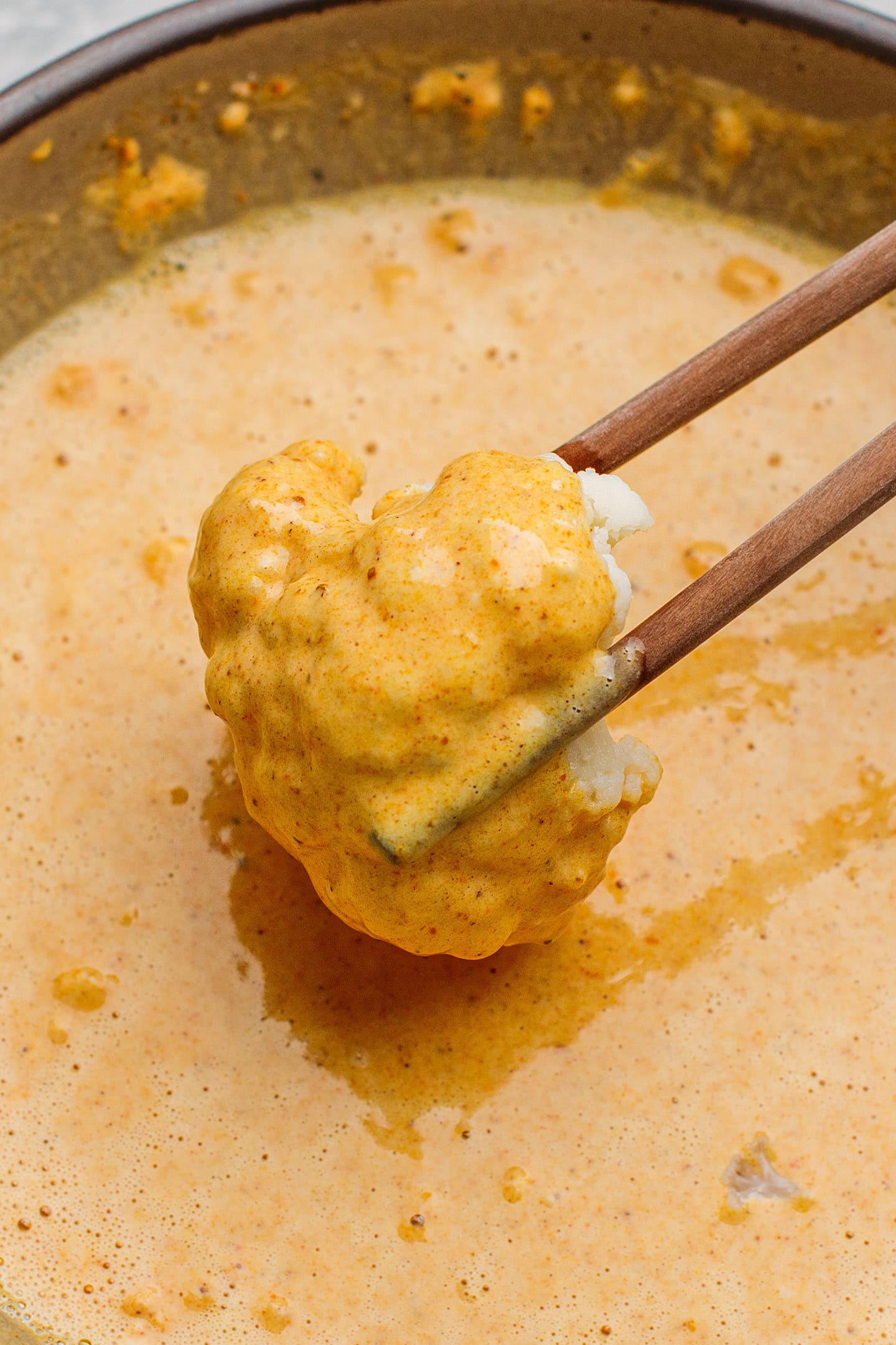 Dipping cauliflower floret into a tempura batter.