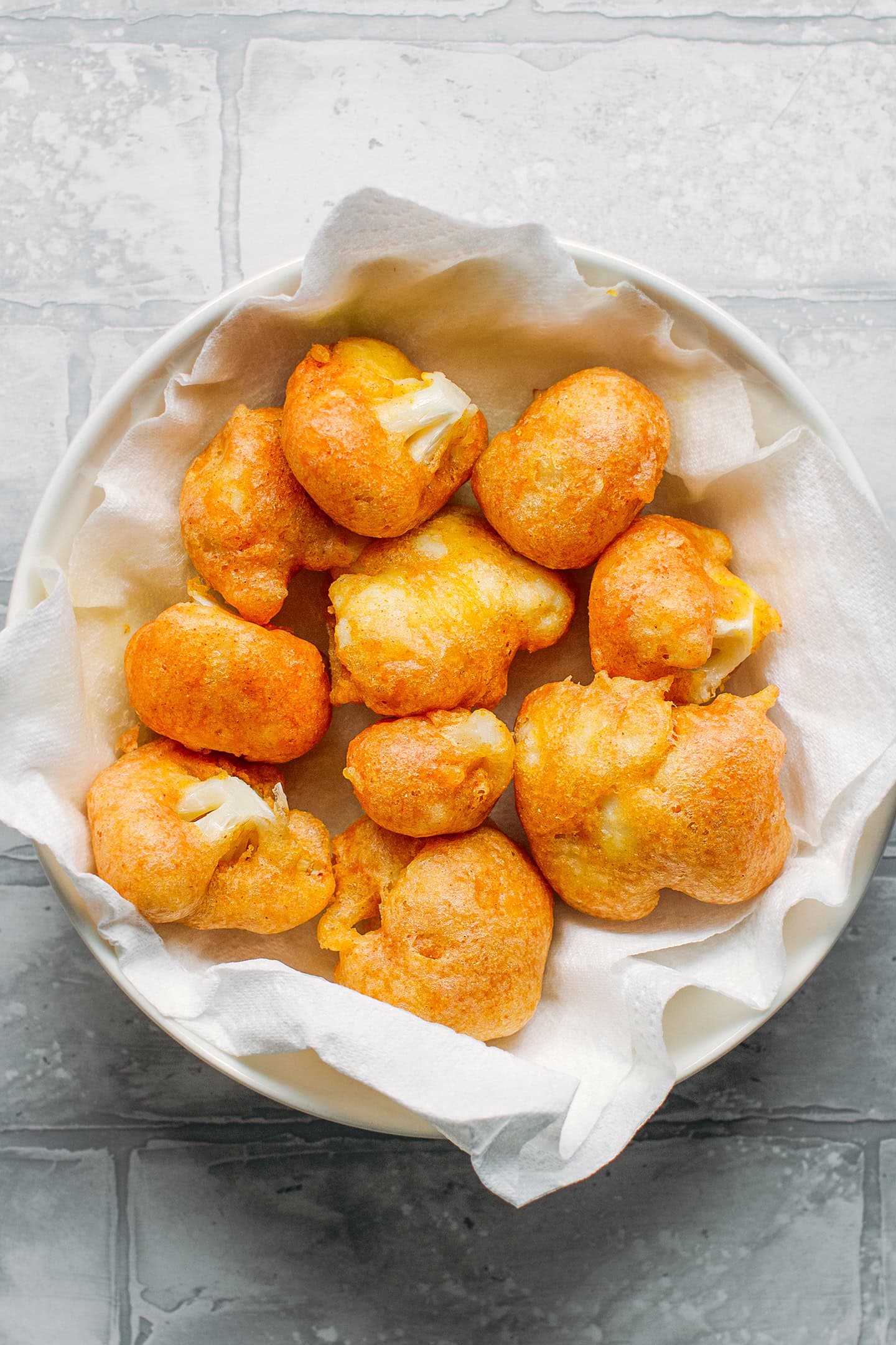 Cauliflower tempura on a plate lined with kitchen paper towels.