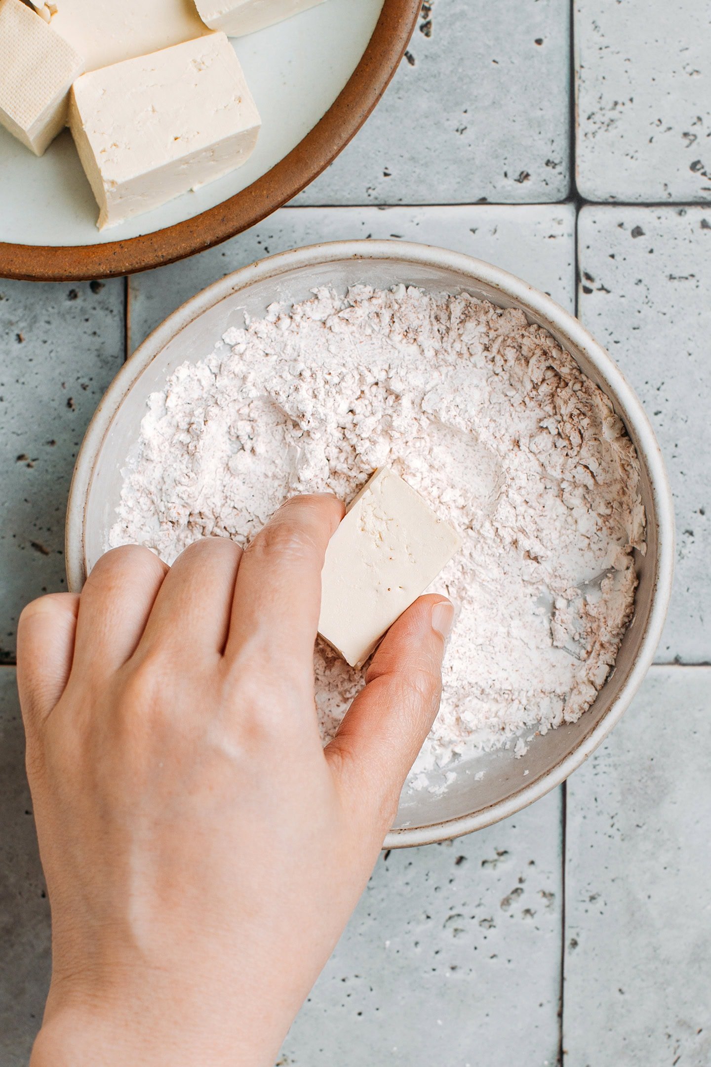 Adding a cube of tofu to a bowl of cornstarch.