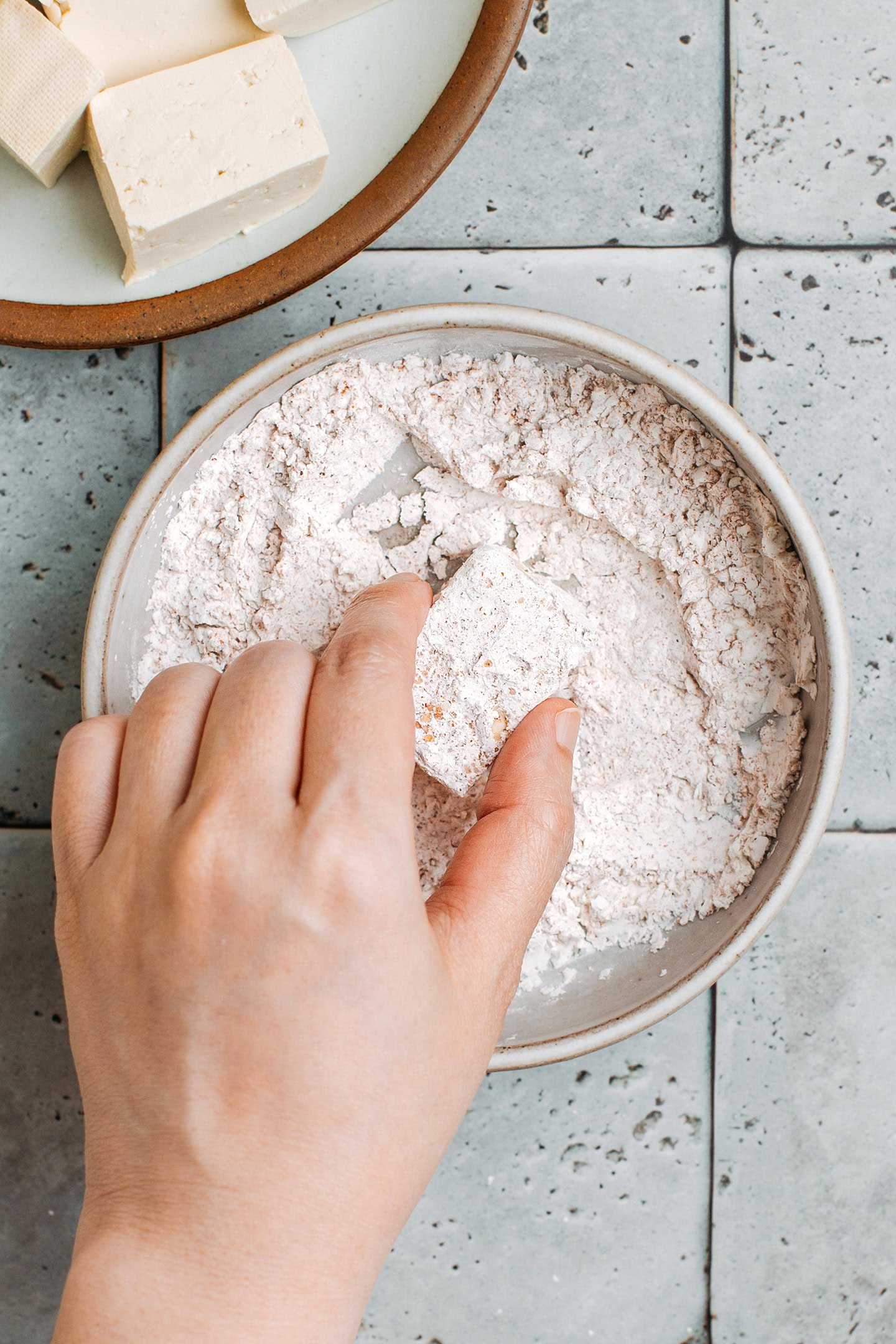 Tossing a cube of tofu in cornstarch.