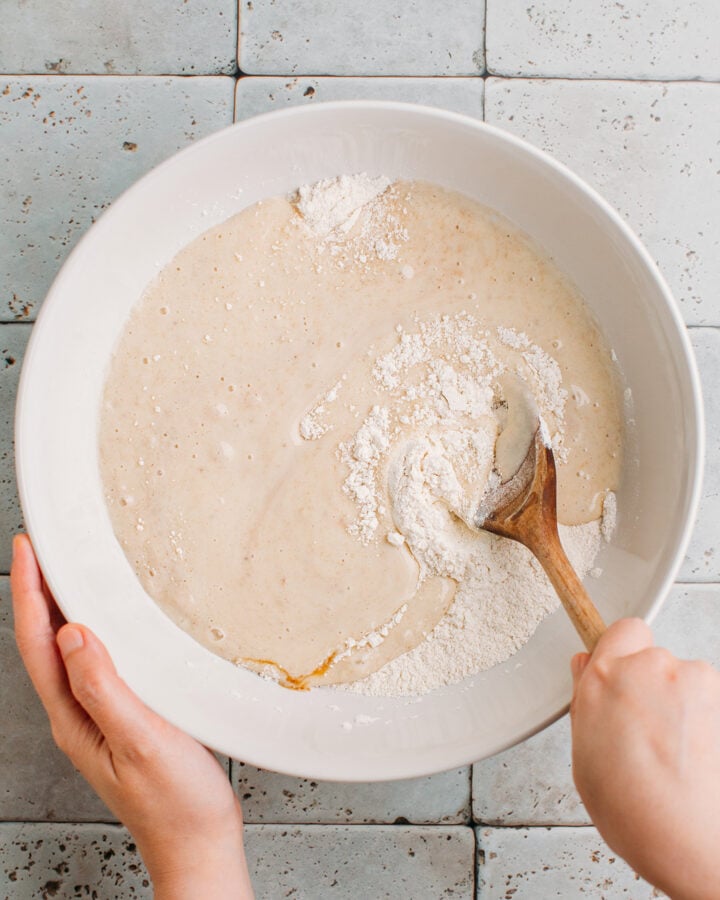Mixing blended bananas with flour and sugar in a bowl.