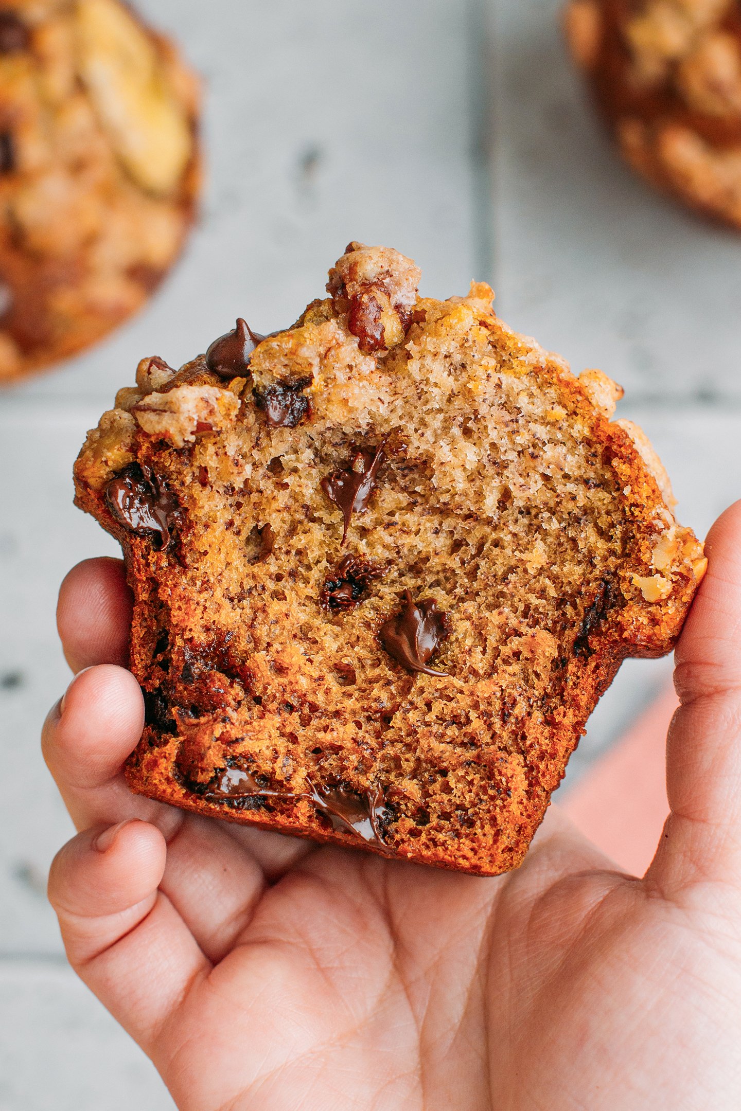 Holding a halve of banana muffin packed with chocolate chips.