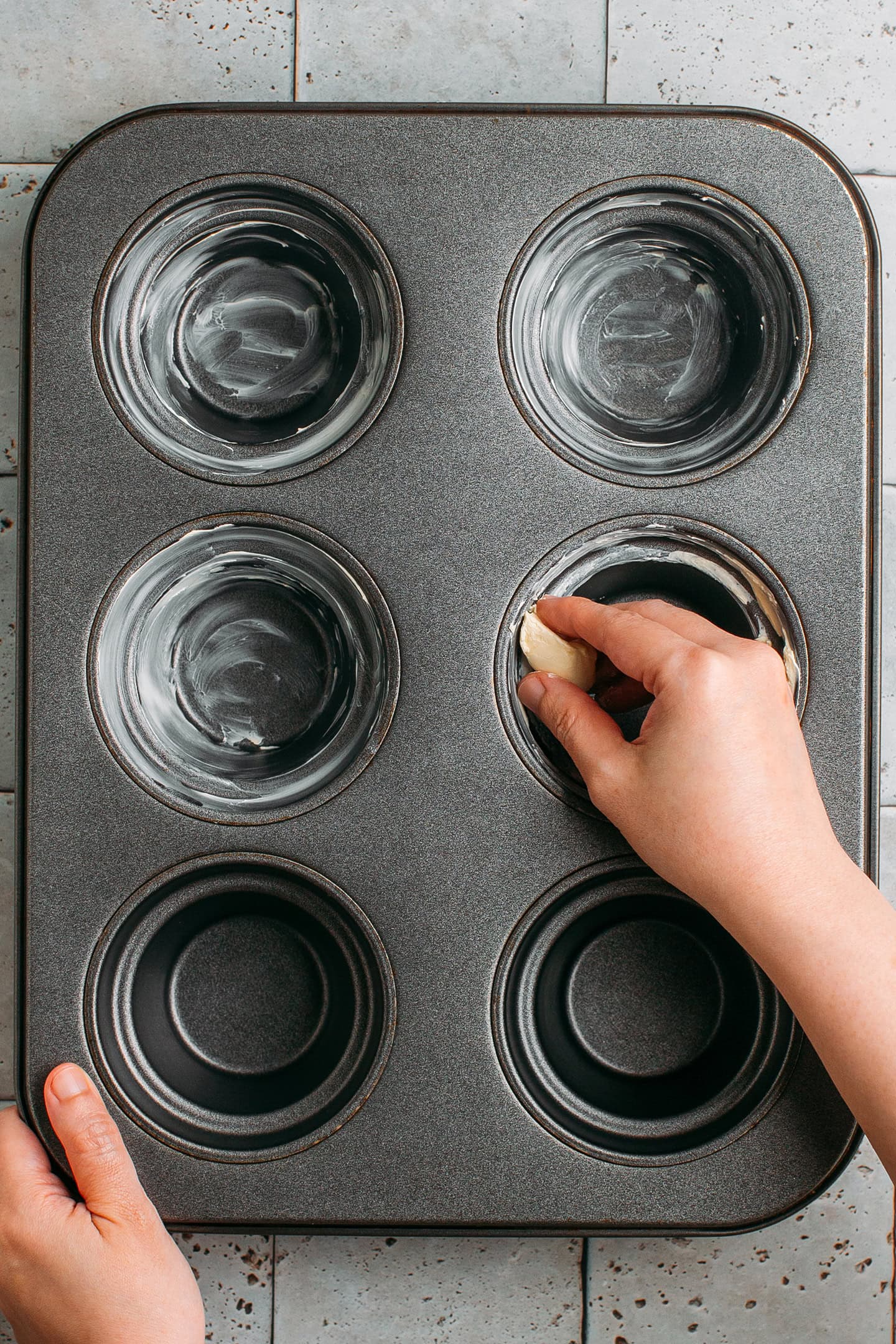 Greasing a muffin pan with butter.