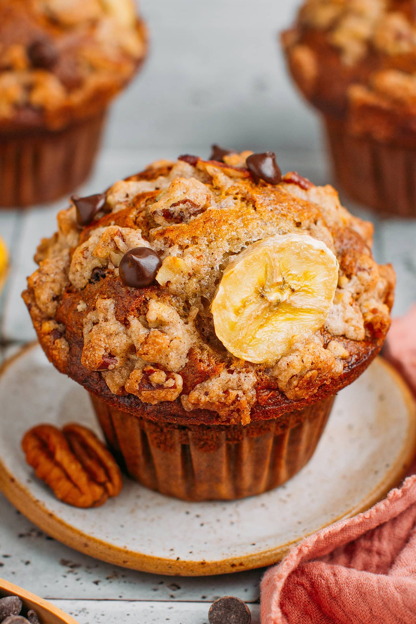 Vegan banana muffin topped with chocolate chips and a pecan streusel on a small plate.