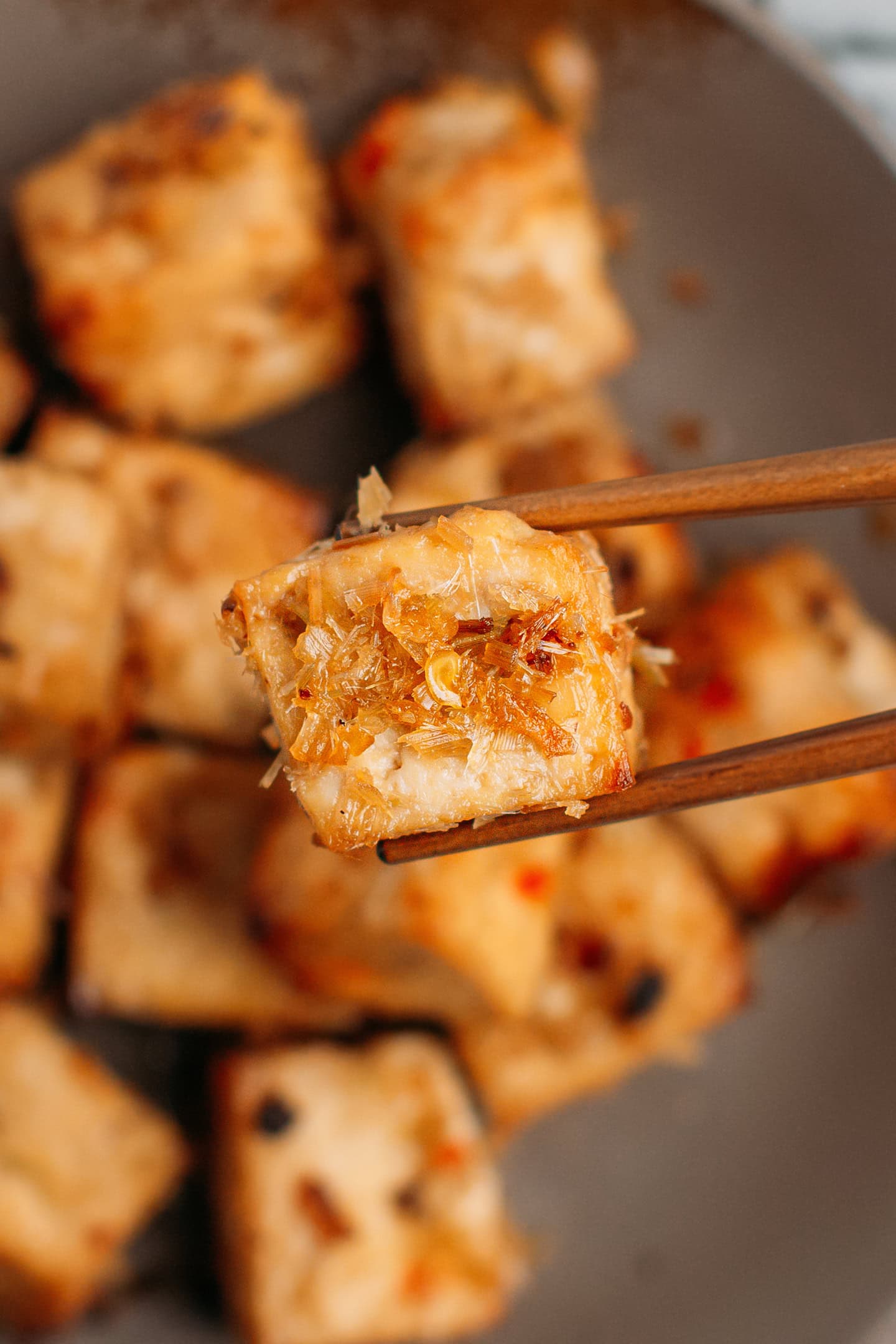 Close-up of a holding a cube of lemongrass tofu using chopsticks.