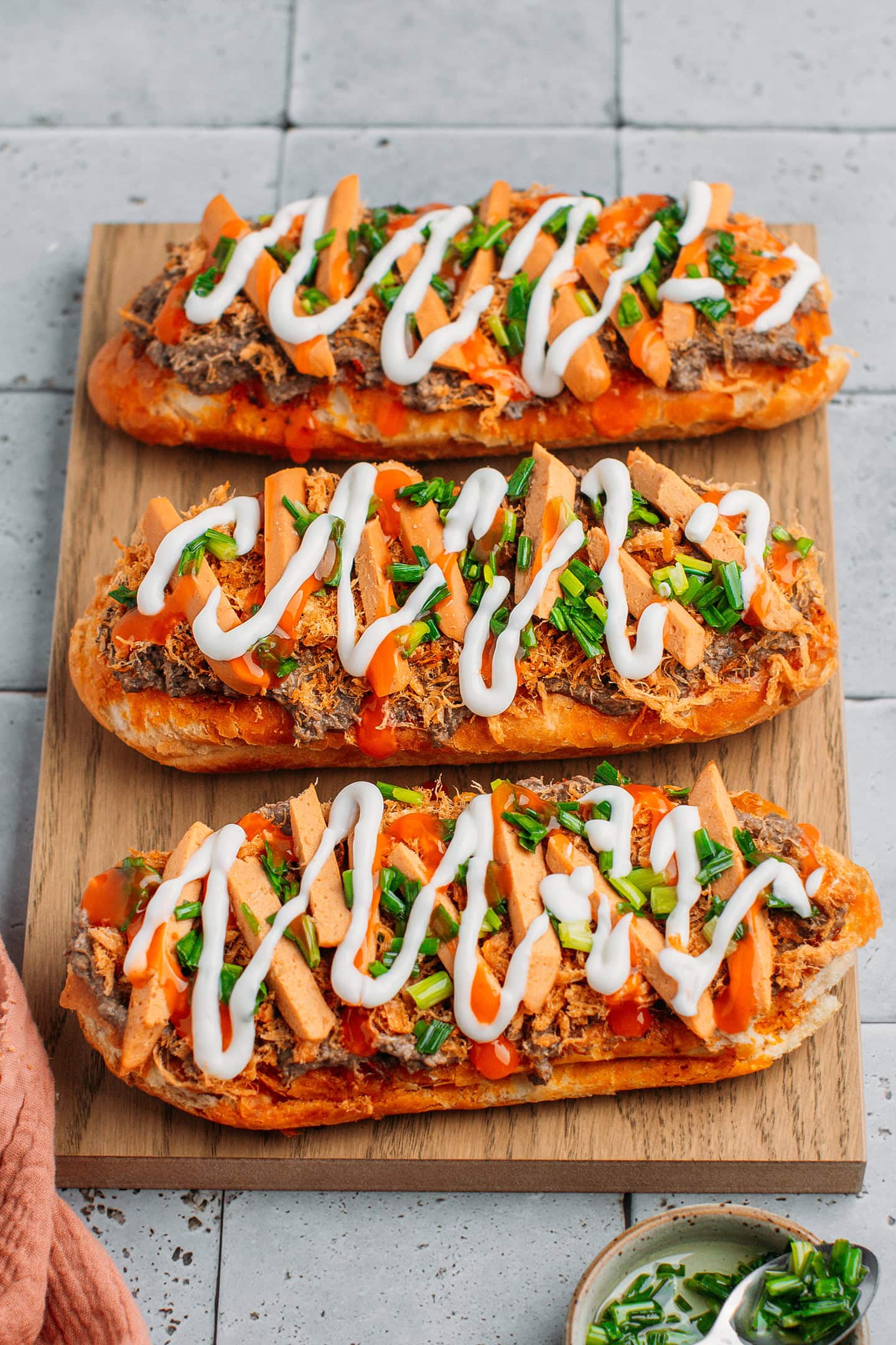 Grilled banh mi bread topped with pâté, sausages, green onions, sweet chili sauce, and mayo.
