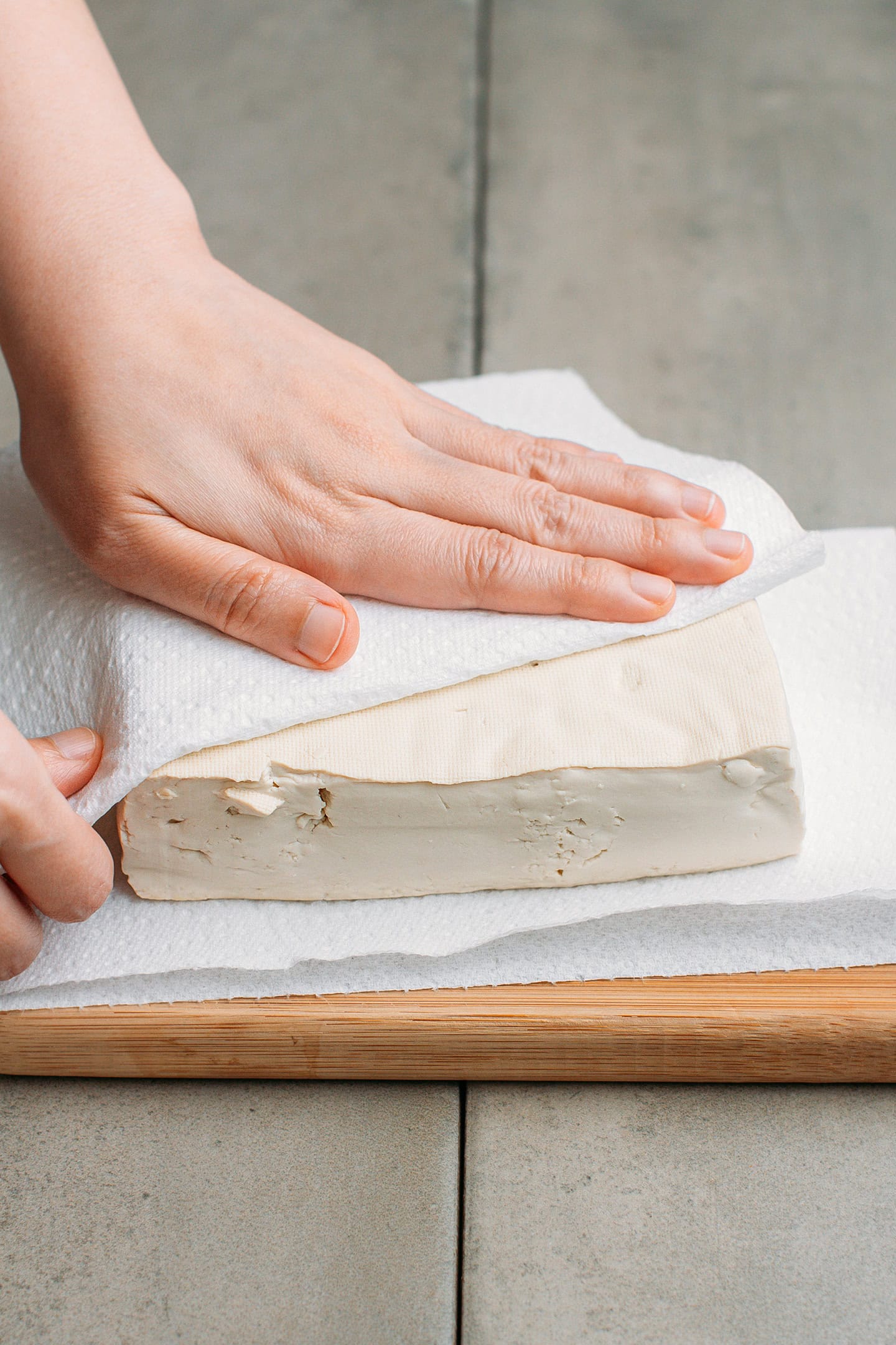 Pressing tofu between two layers of kitchen paper towels.