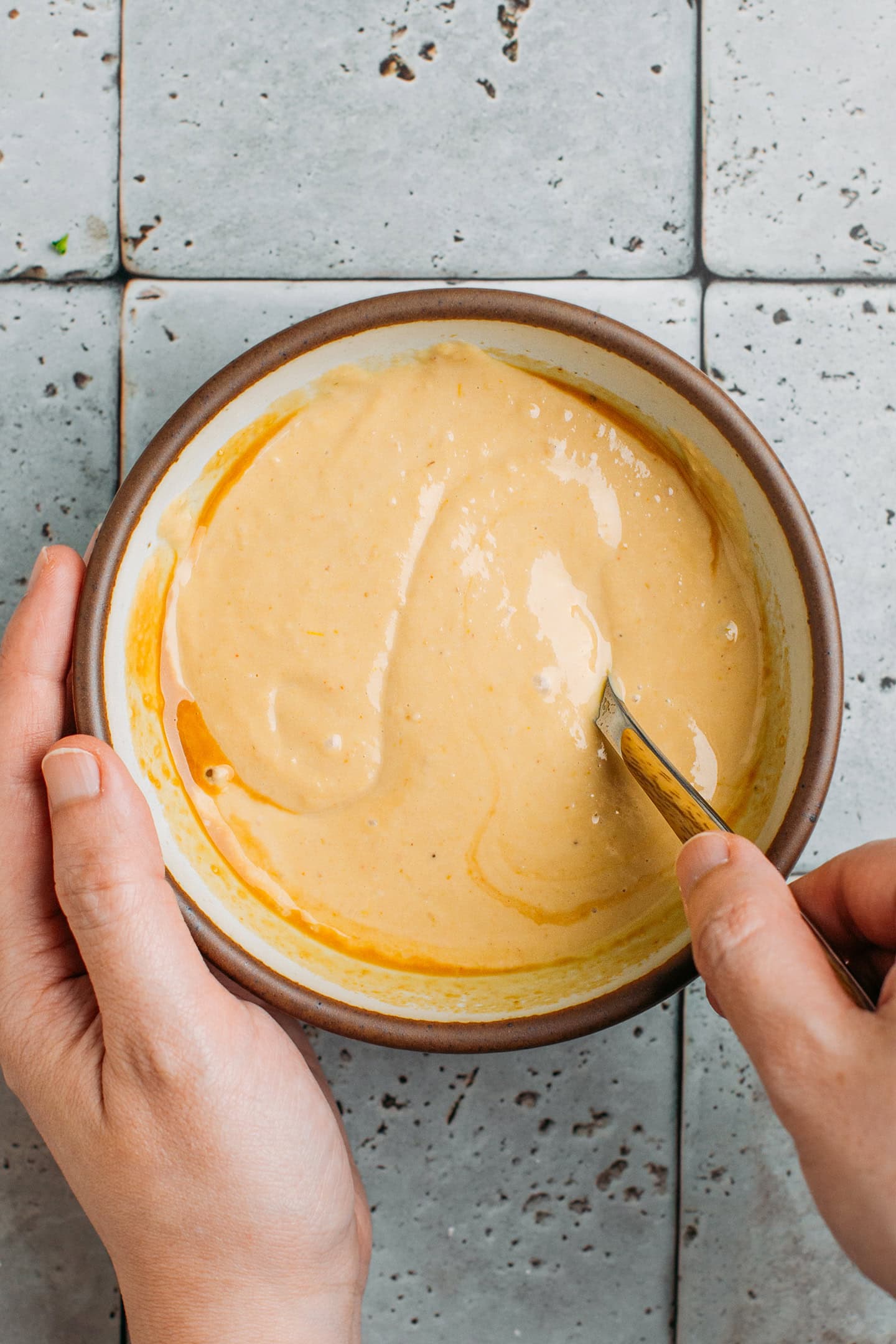 Stirring hummus with green curry paste in a bowl.