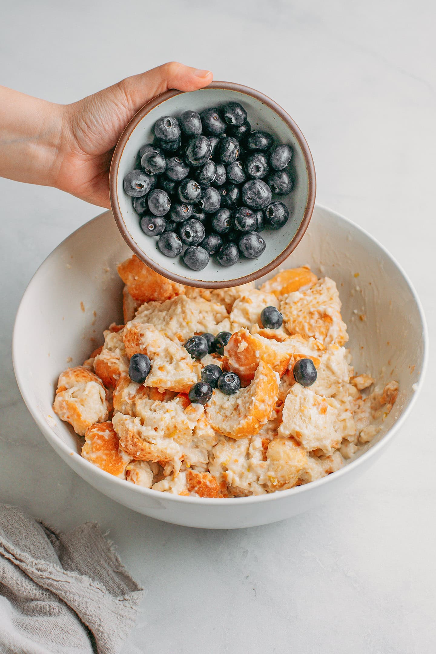 Adding blueberries to a bowl of diced bread.