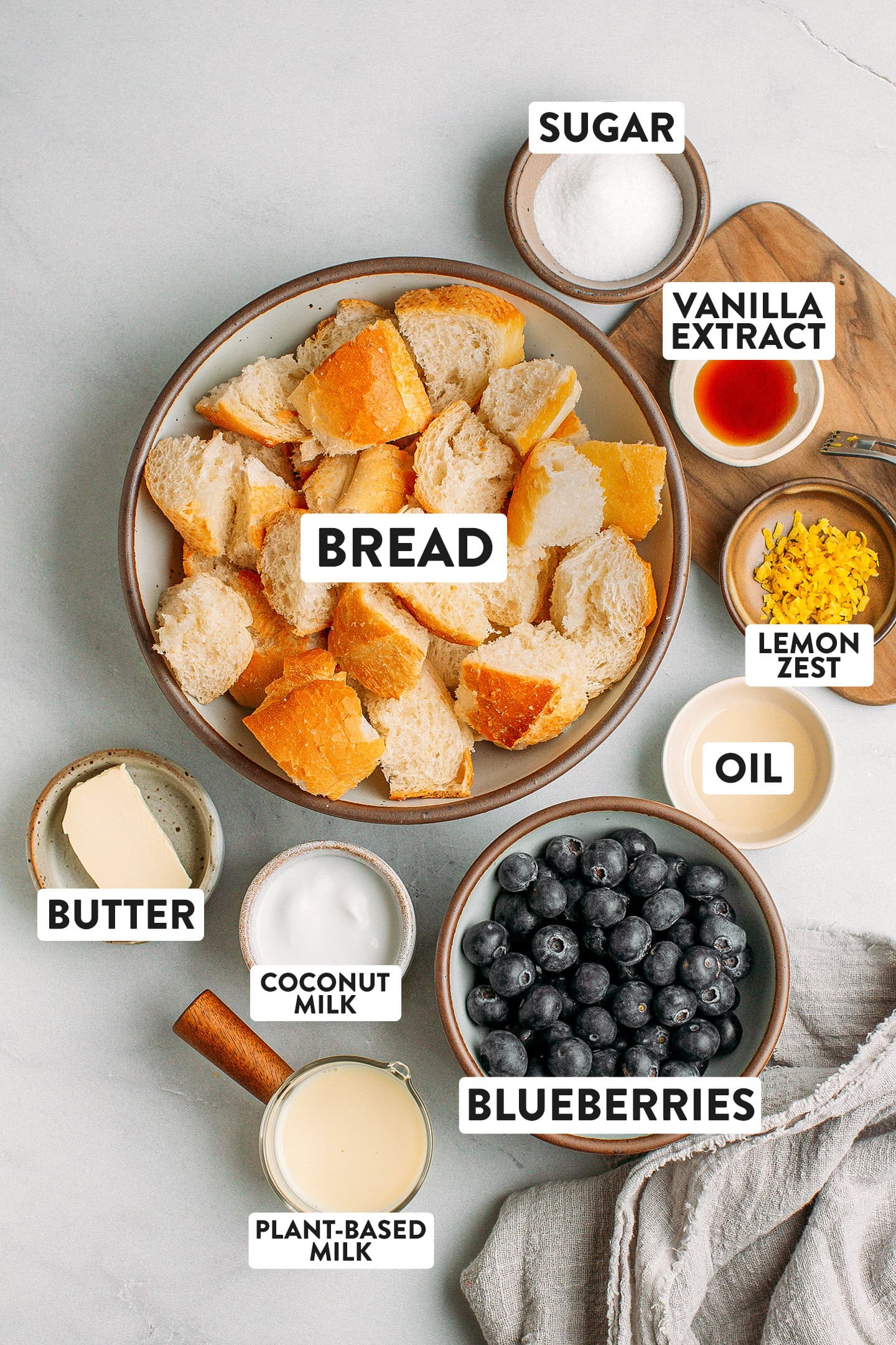 Ingredients like diced bread, blueberries, coconut milk, lemon zest, and sugar.