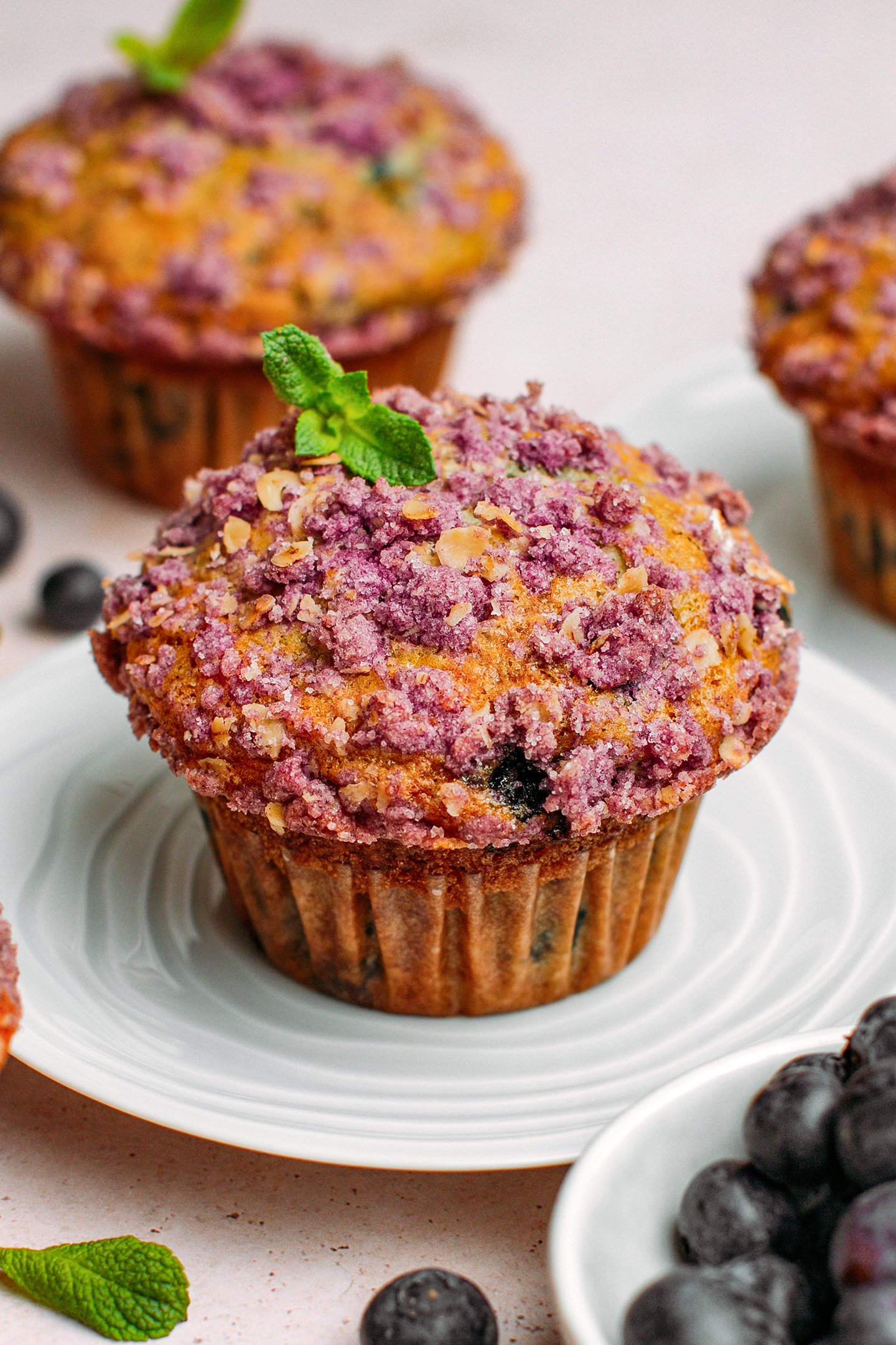 Blueberry muffin topped with streusel and mint on a small plate.