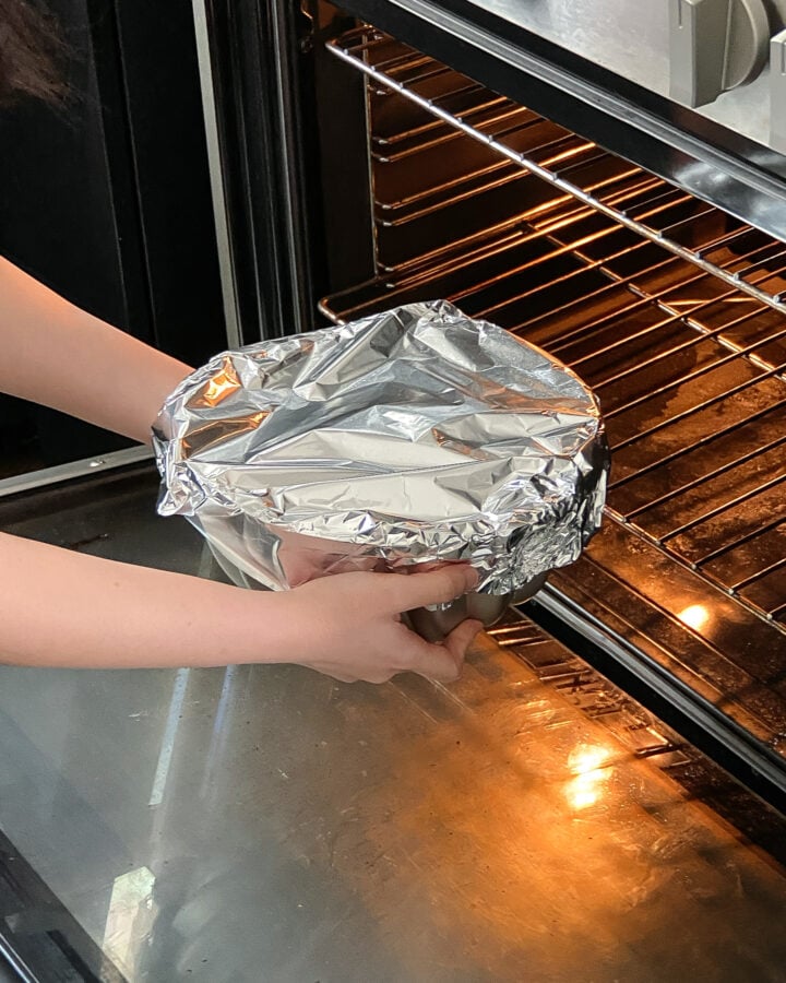 Placing a bundt cake covered with aluminum foil in the oven.