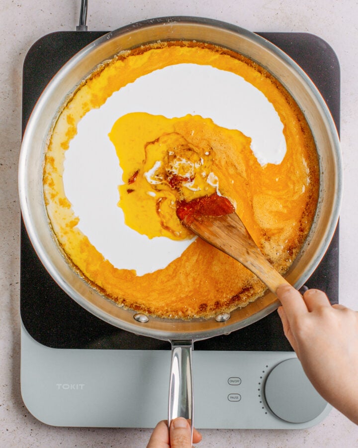 Stirring coconut milk into caramel in a large pan.