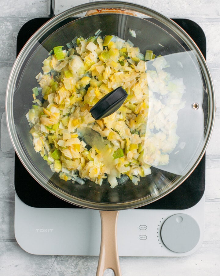 Chopped leeks cooking in a skillet with the lid on.