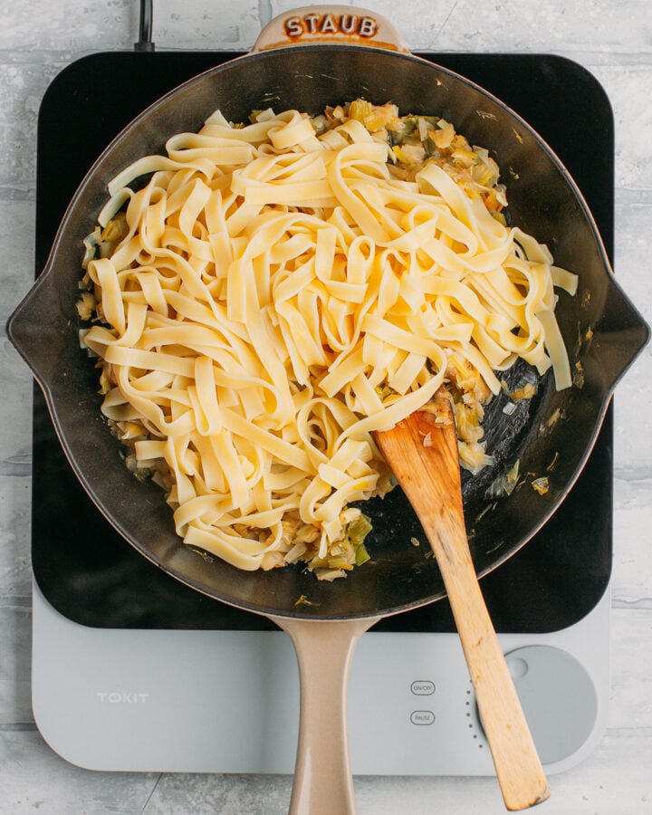 Tagliatelle pasta and sautéed leeks in a pan.