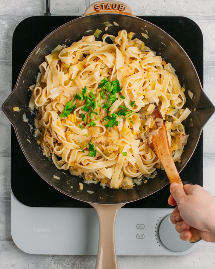 Tossing tagliatelle pasta with sautéed leeks and parsley.