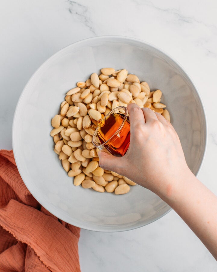 Pouring maple syrup into a bowl containing blanched almonds.