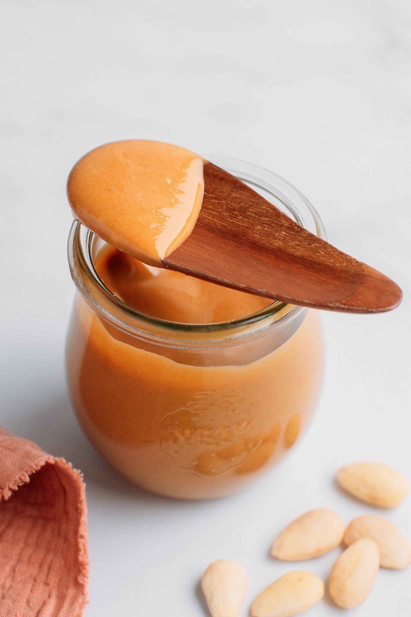 Wooden spoon filled with almond butter on top of a jar of almond butter.