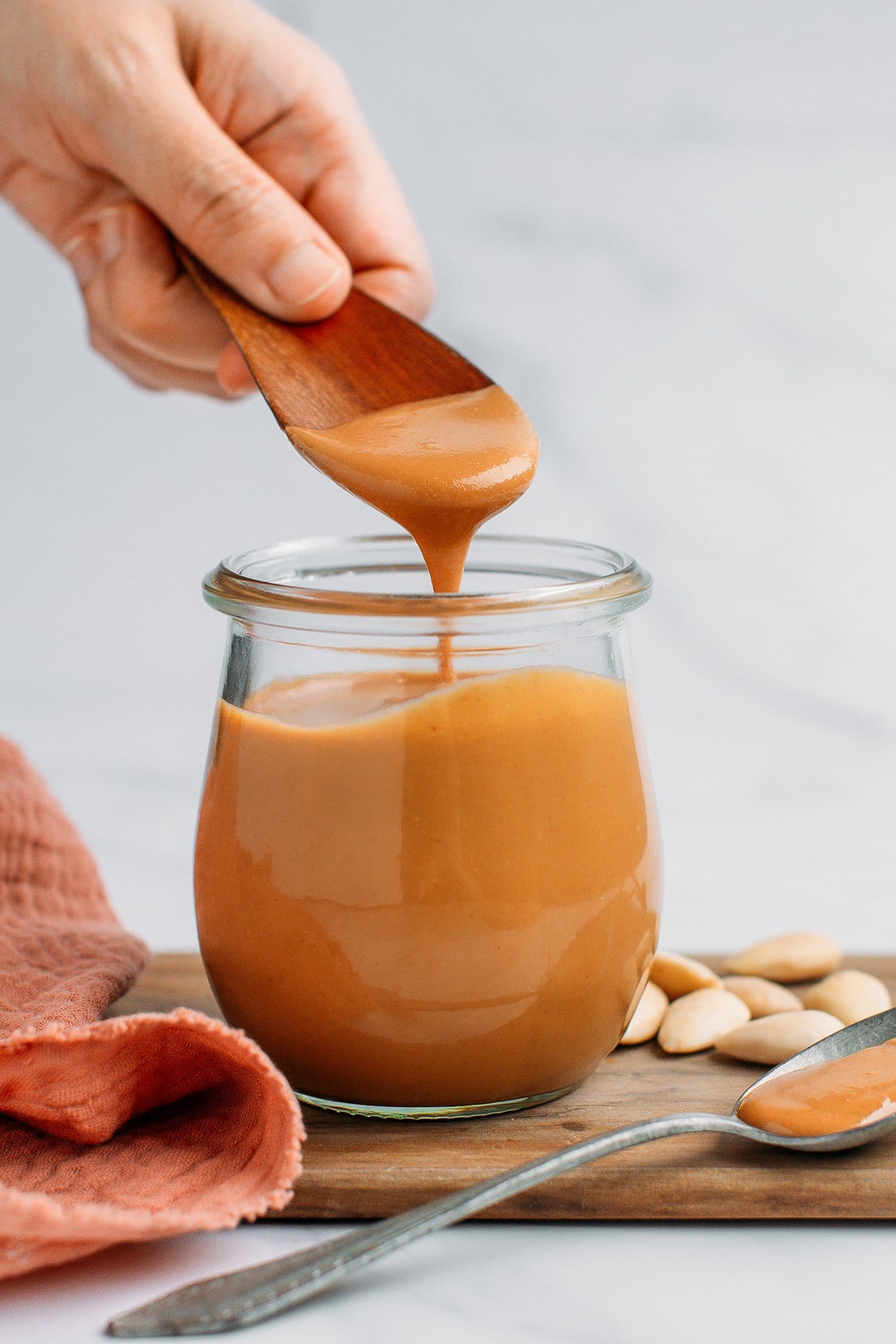 Holding a wooden spoon full of almond butter over a jar.