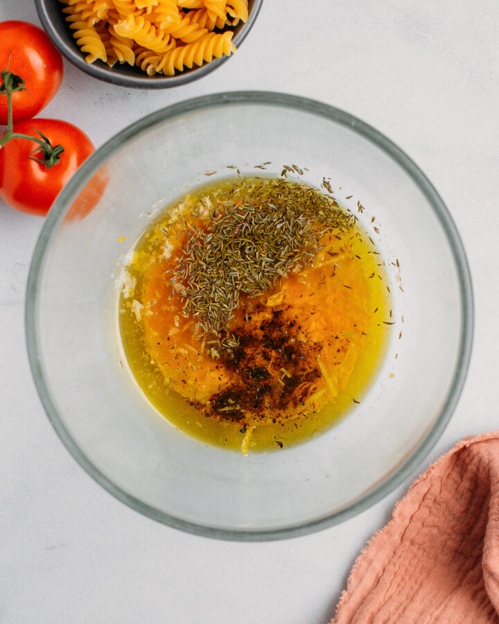 Olive oil, mustard, lemon juice, thyme, and black pepper in a bowl.
