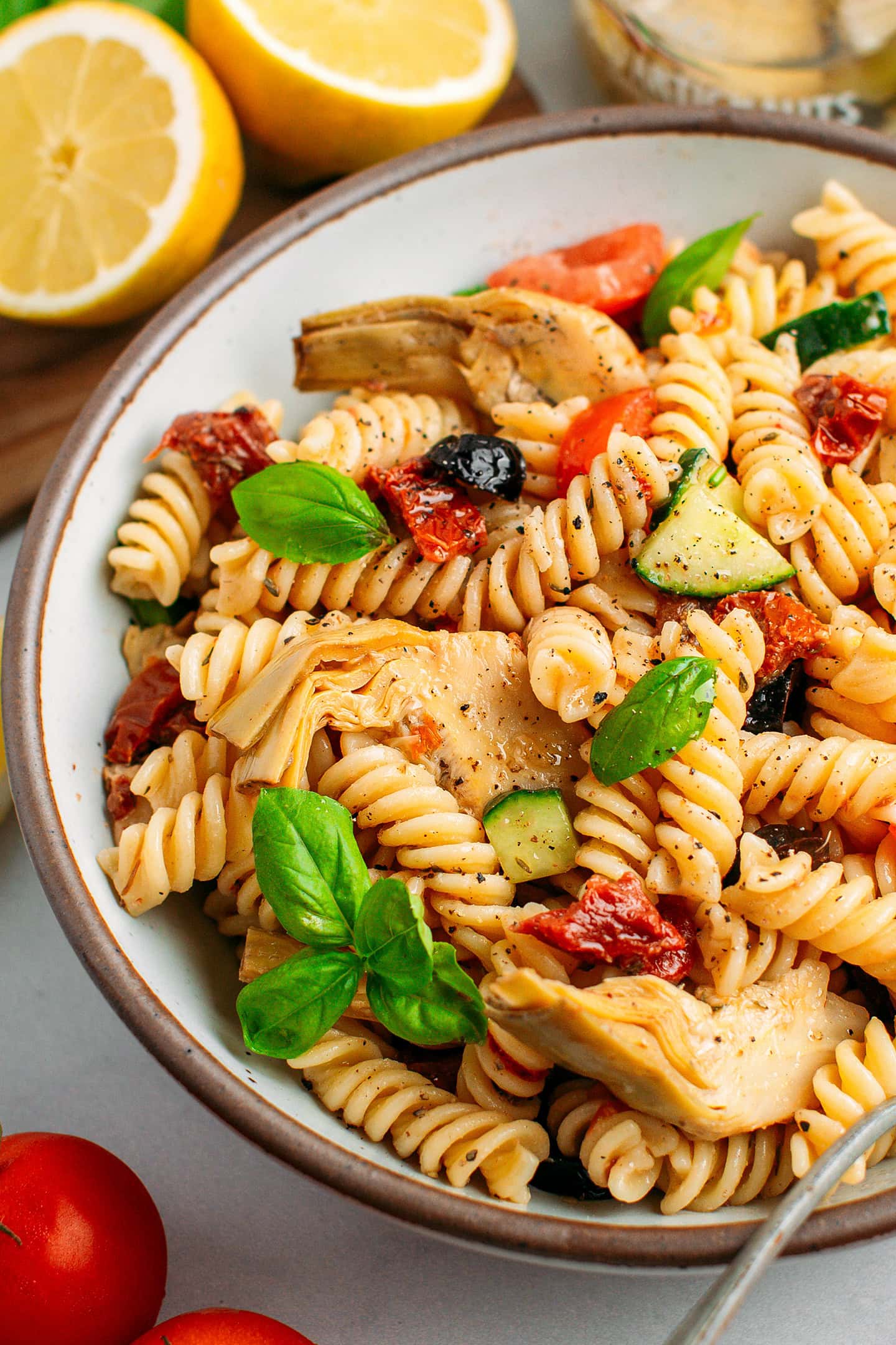 Close-up of pasta salad with grilled artichoke hearts, sun-dried tomatoes, and diced cucumber.