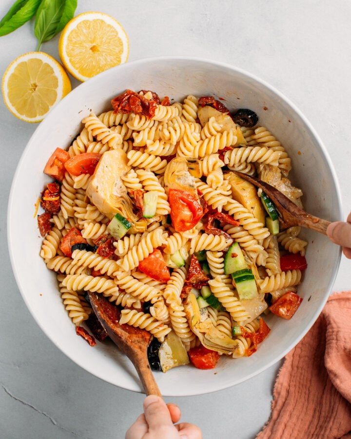 Mixing pasta salad in a bowl using two wooden spoons.