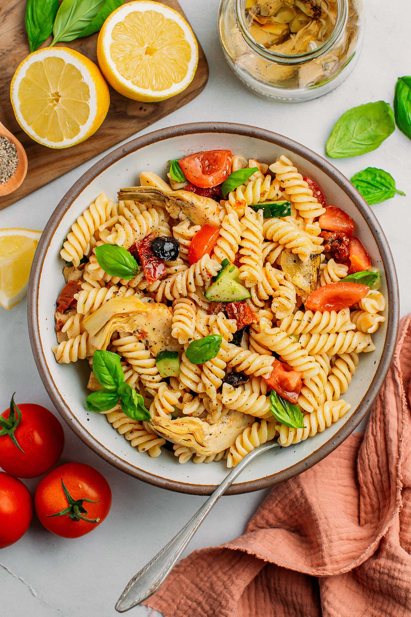 Fusilli pasta salad with sun-dried tomatoes, olives, and artichoke hearts in a deep plate.