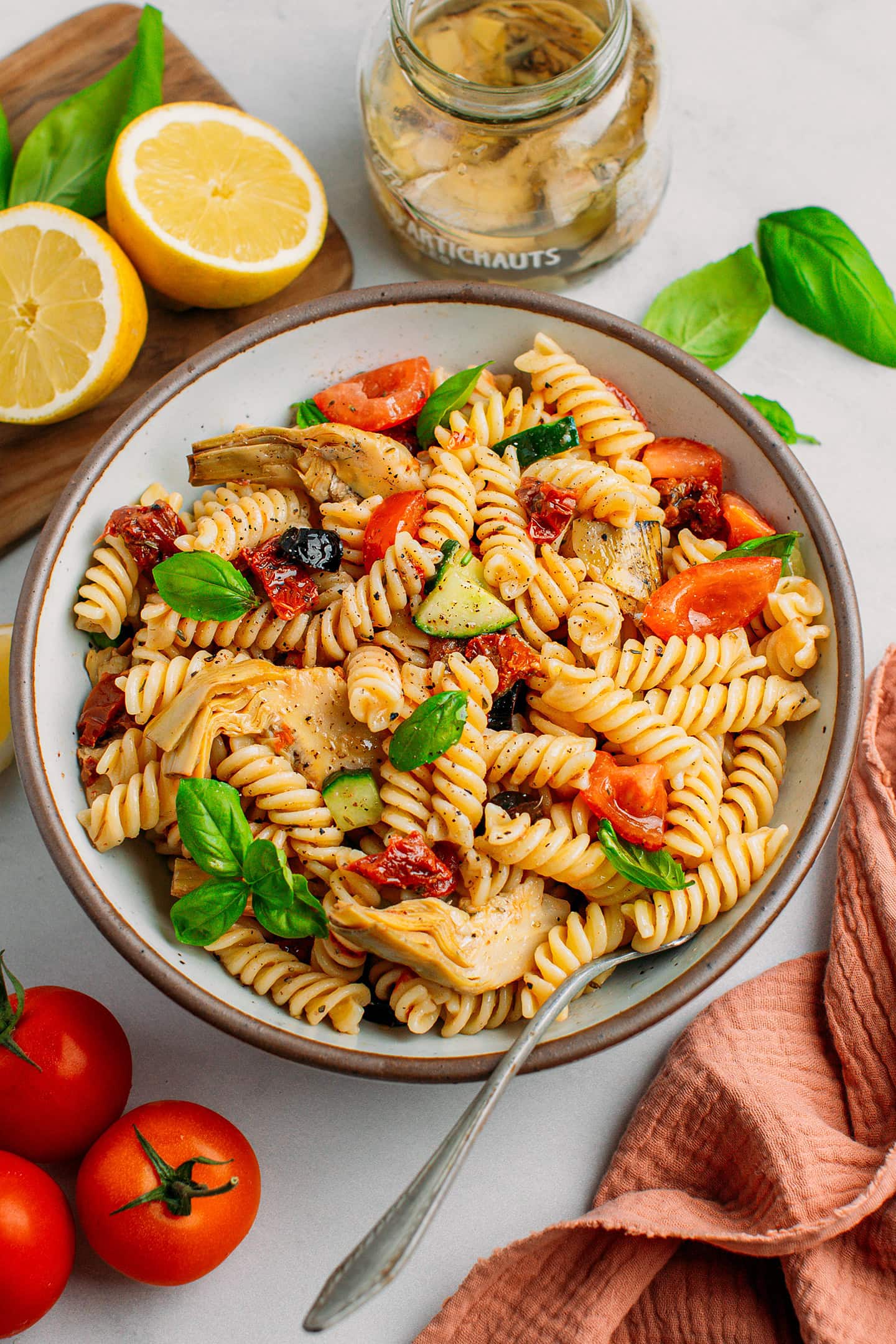 Pasta salad with diced cucumber, artichoke hearts, sun-dried tomatoes, and olives in a deep plate.