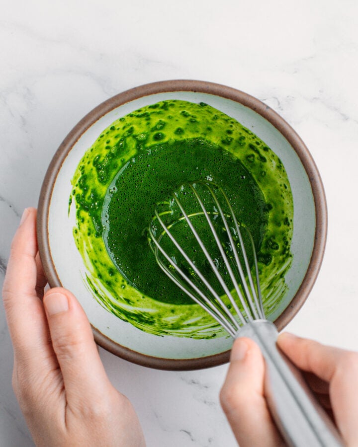 Whisking matcha powder and water in a small bowl.