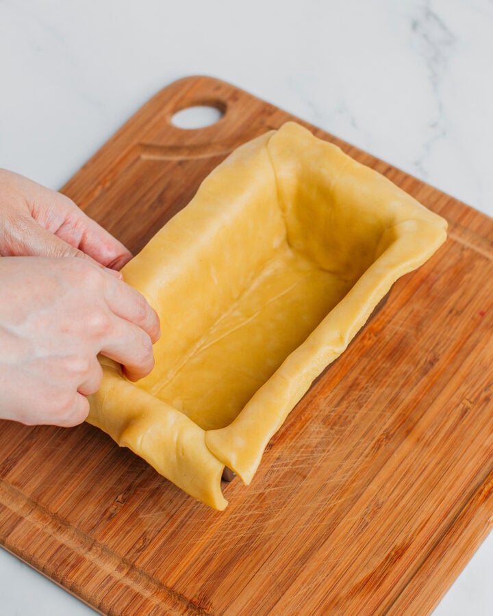 Pressing pie crust into a terrine baking pan.