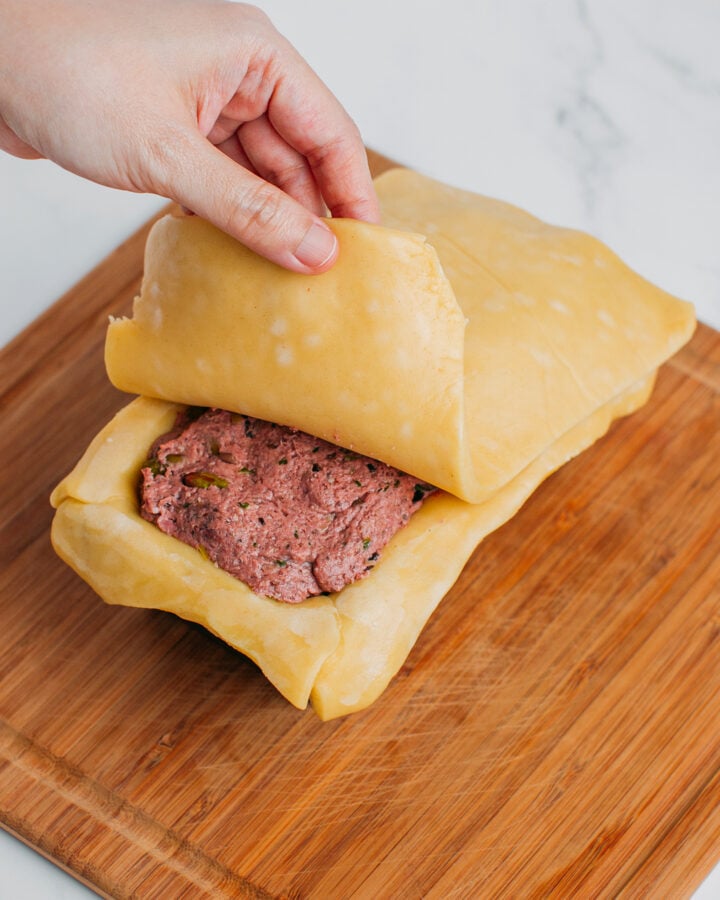 Placing a layer of pie crust on top of a mushroom filling.