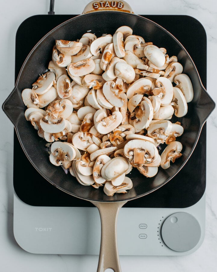 Sliced white button mushrooms in a skillet.