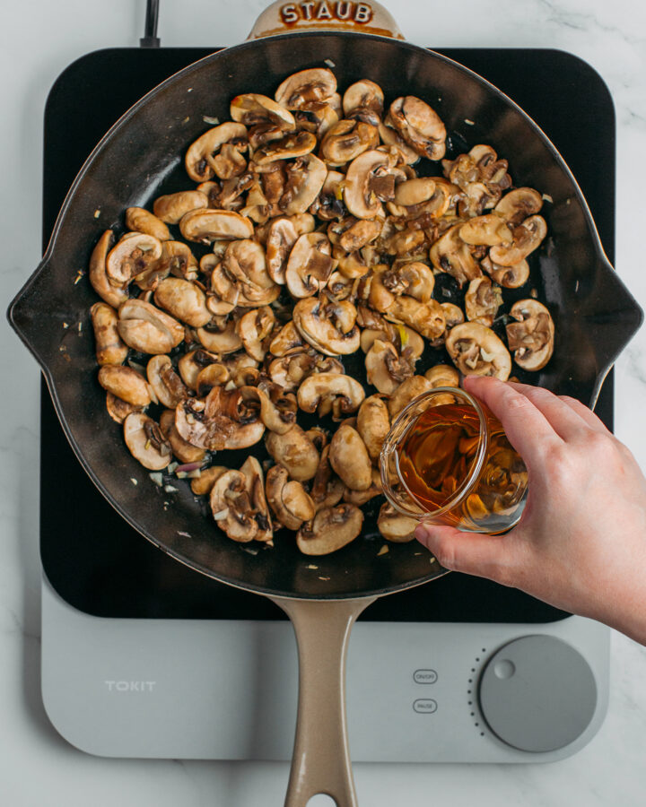 Pouring cognac into a skillet filled with sautéed mushrooms.