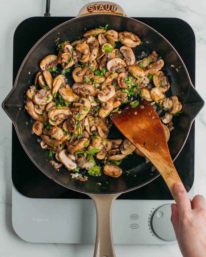Tossing sautéed mushrooms with chopped parsley in a skillet.