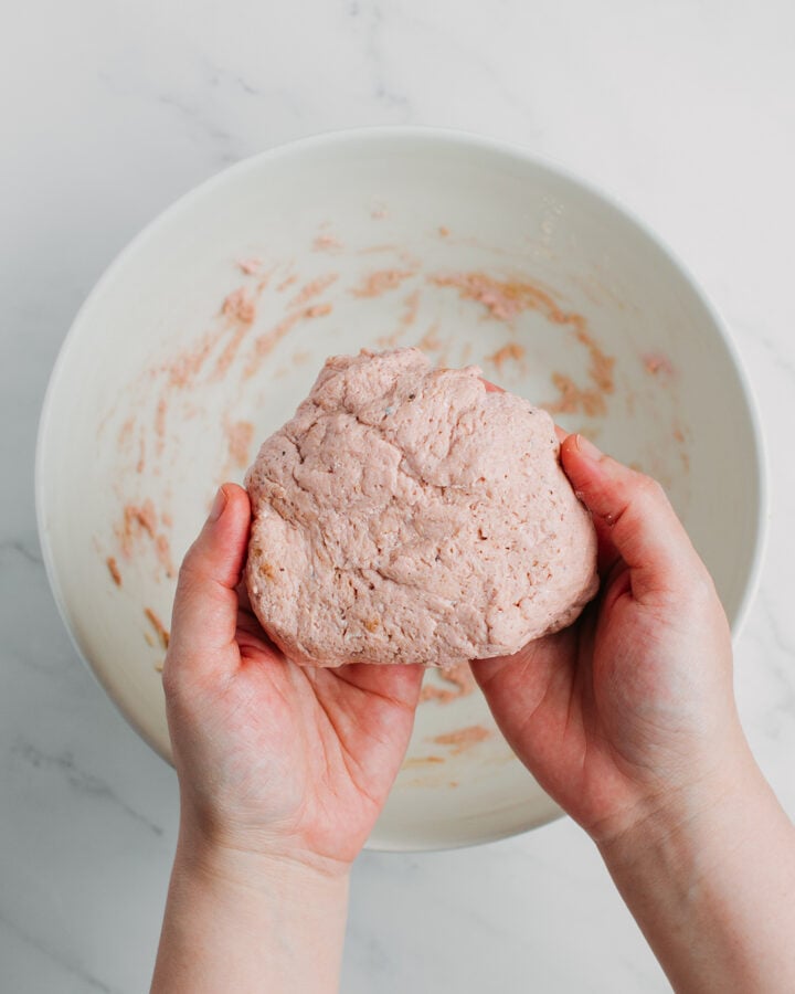 Holding a ball of seitan over a bowl.