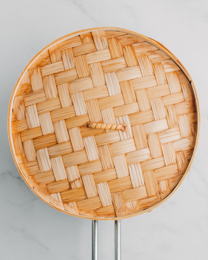 Closed bamboo steamer basket on top of a pot of boiling water.